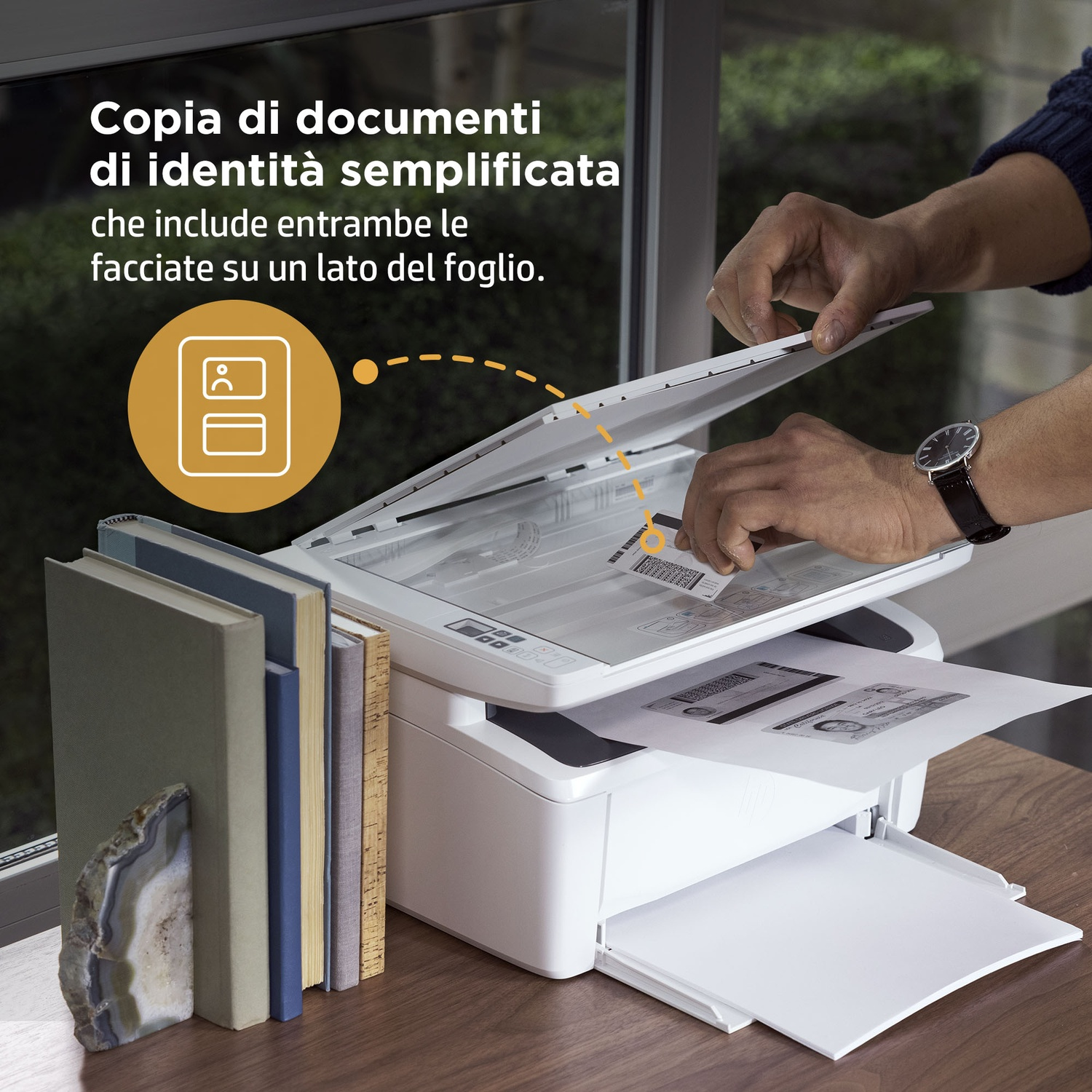 Mani che scansionano documenti su una stampante. Libri e una pietra decorativa sono sul tavolo.