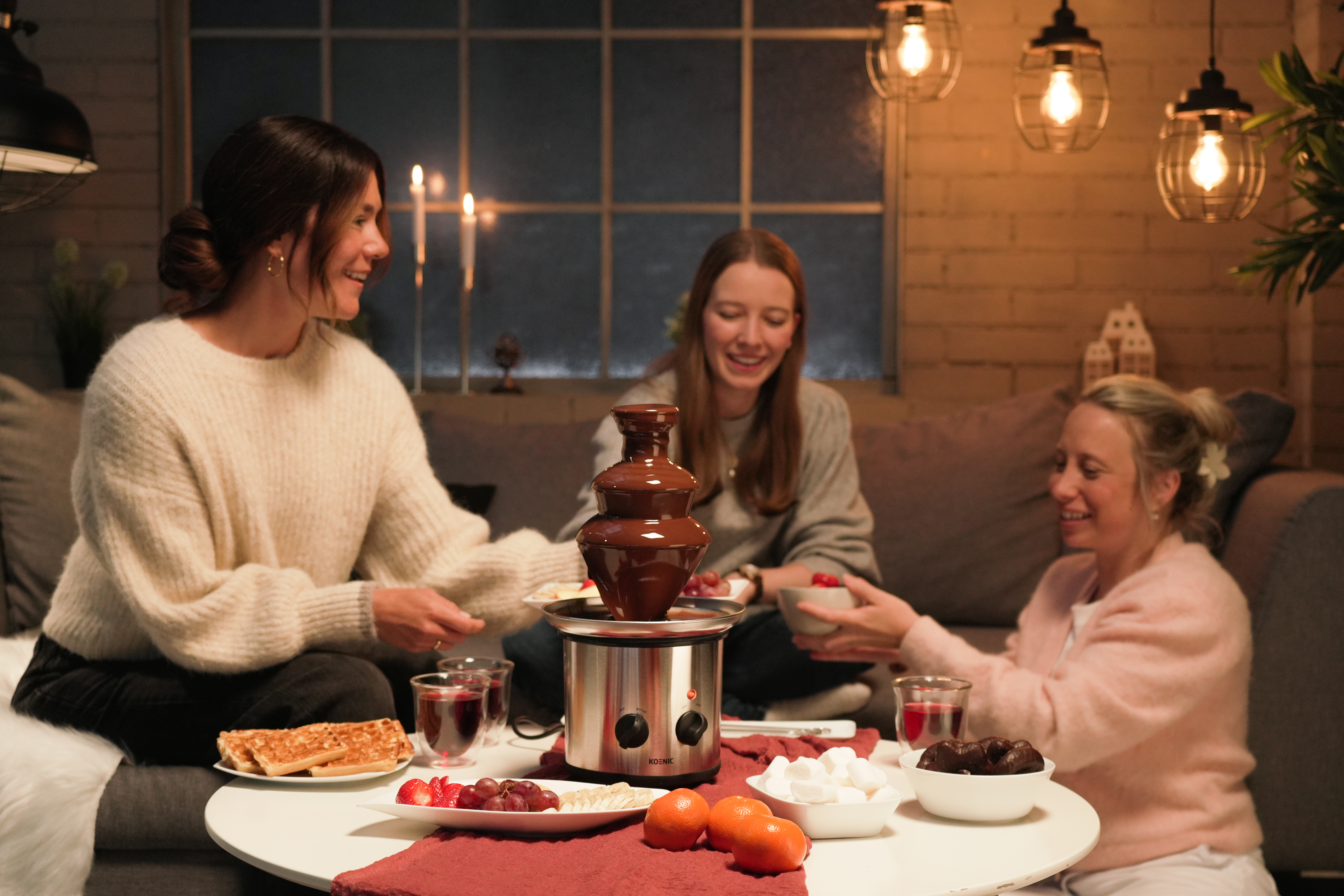 Drei Personen teilen sich Schokoladenfondue. Ein Schokoladenbrunnen steht in der Mitte des Tisches.
