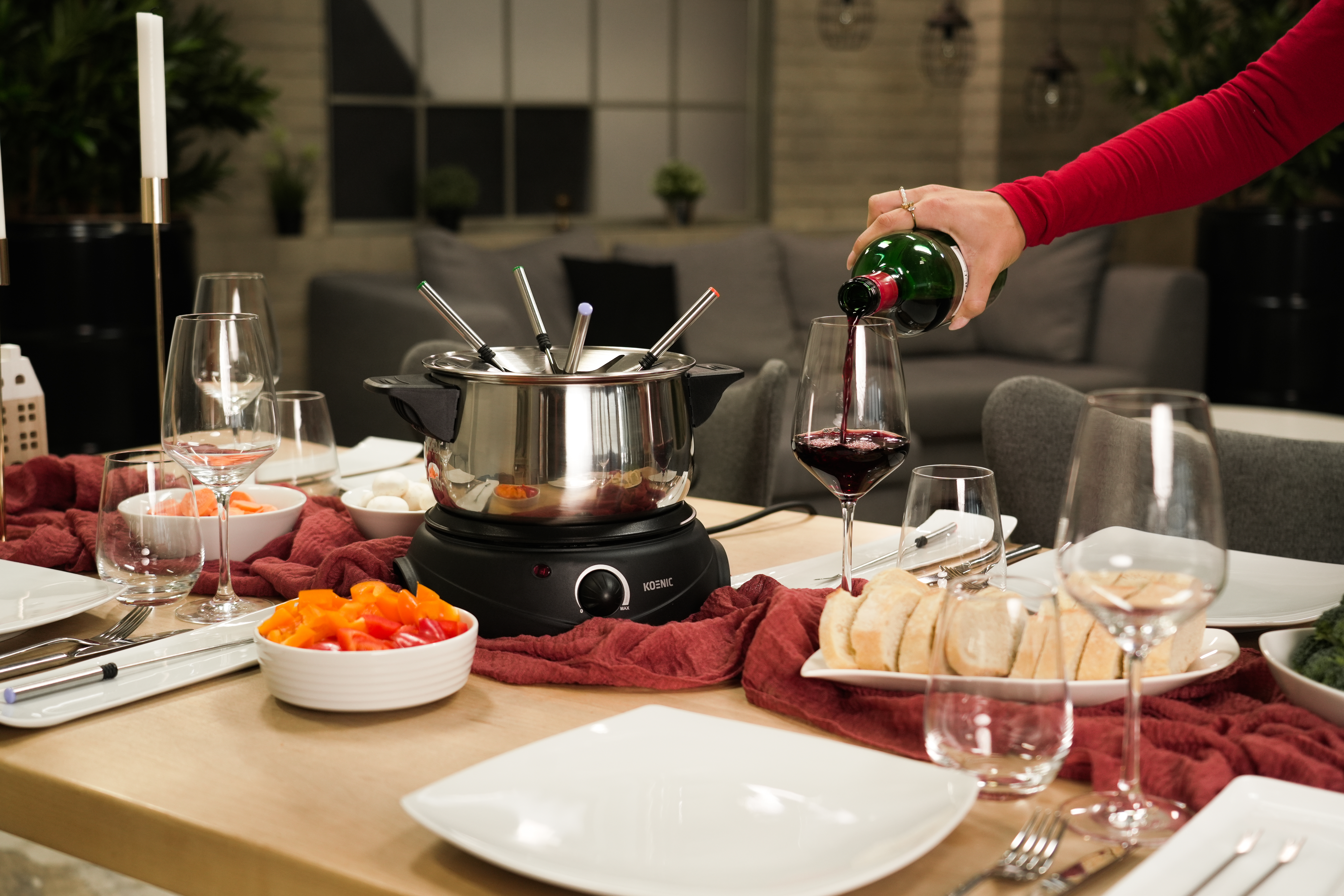 Tisch für Fondue, Person gießt Wein ein. Mit Essen und Gläsern.