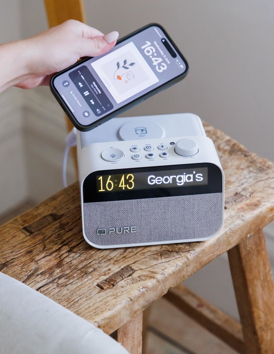 Un téléphone affichant une application musicale est placé sur un haut-parleur sur un tabouret en bois. L'heure est 16:43.