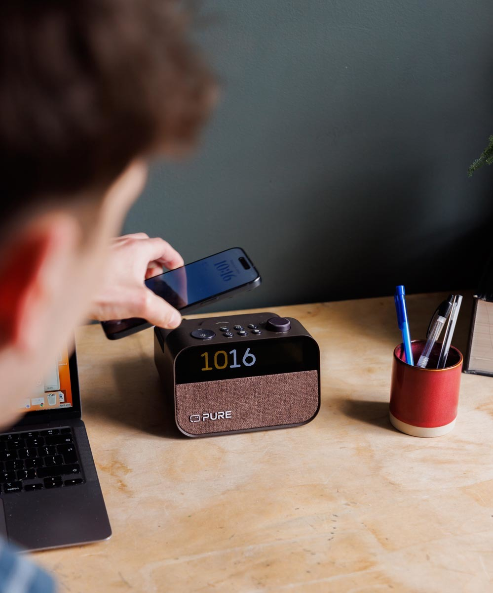Une personne utilise un téléphone près d'une radio. Un porte-stylo et un ordinateur portable sur le bureau en bois.
