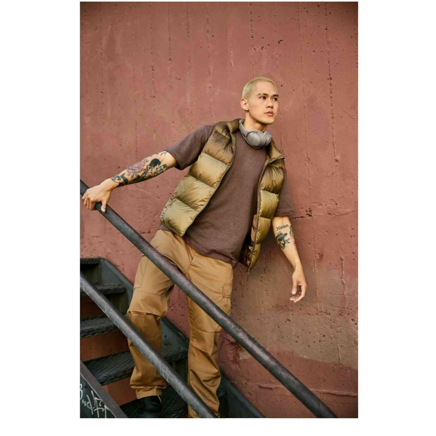 Man in a brown outfit with headphones on a staircase.  Red wall.