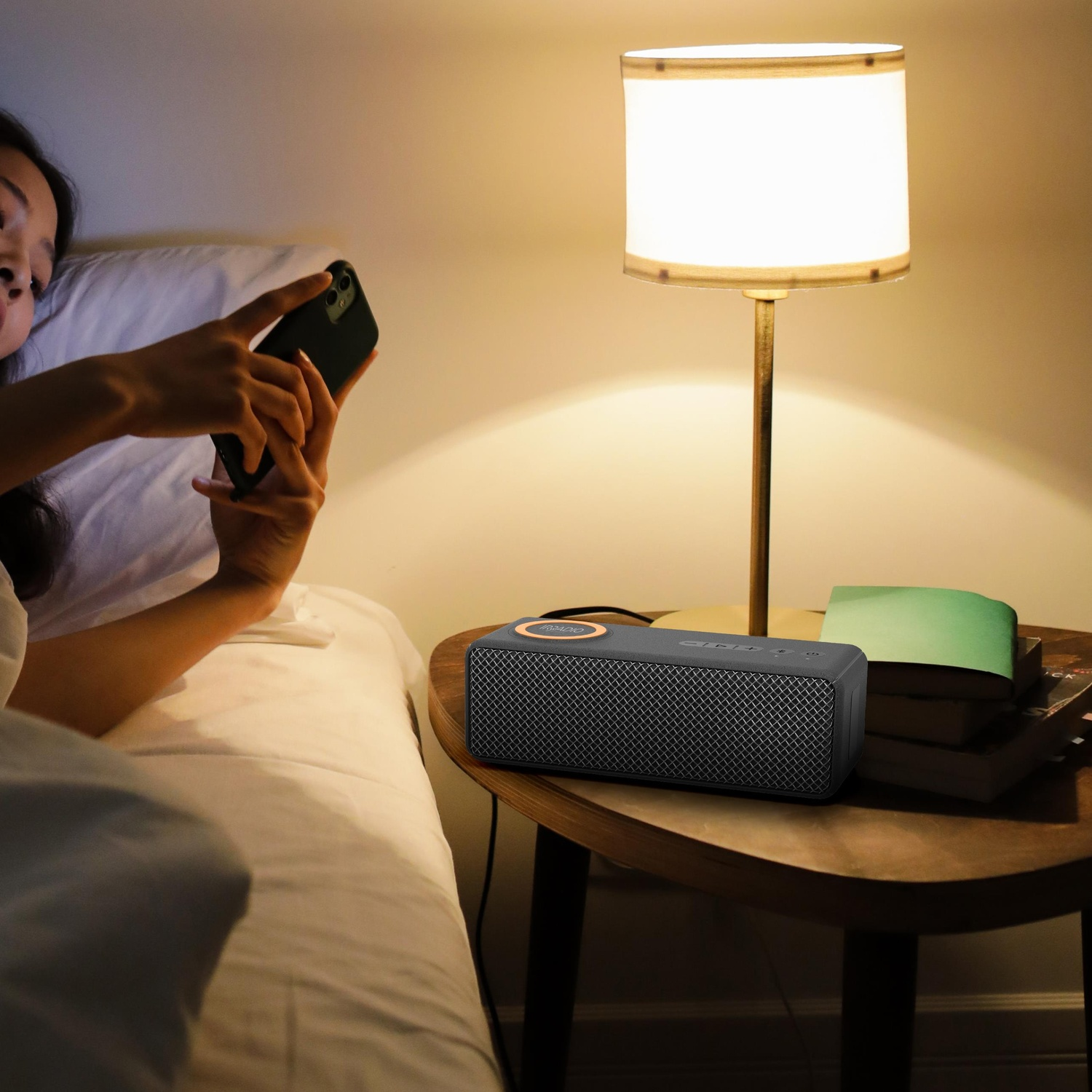 Donna a letto che usa lo smartphone. Altoparlante sul comodino. Lampada accesa.