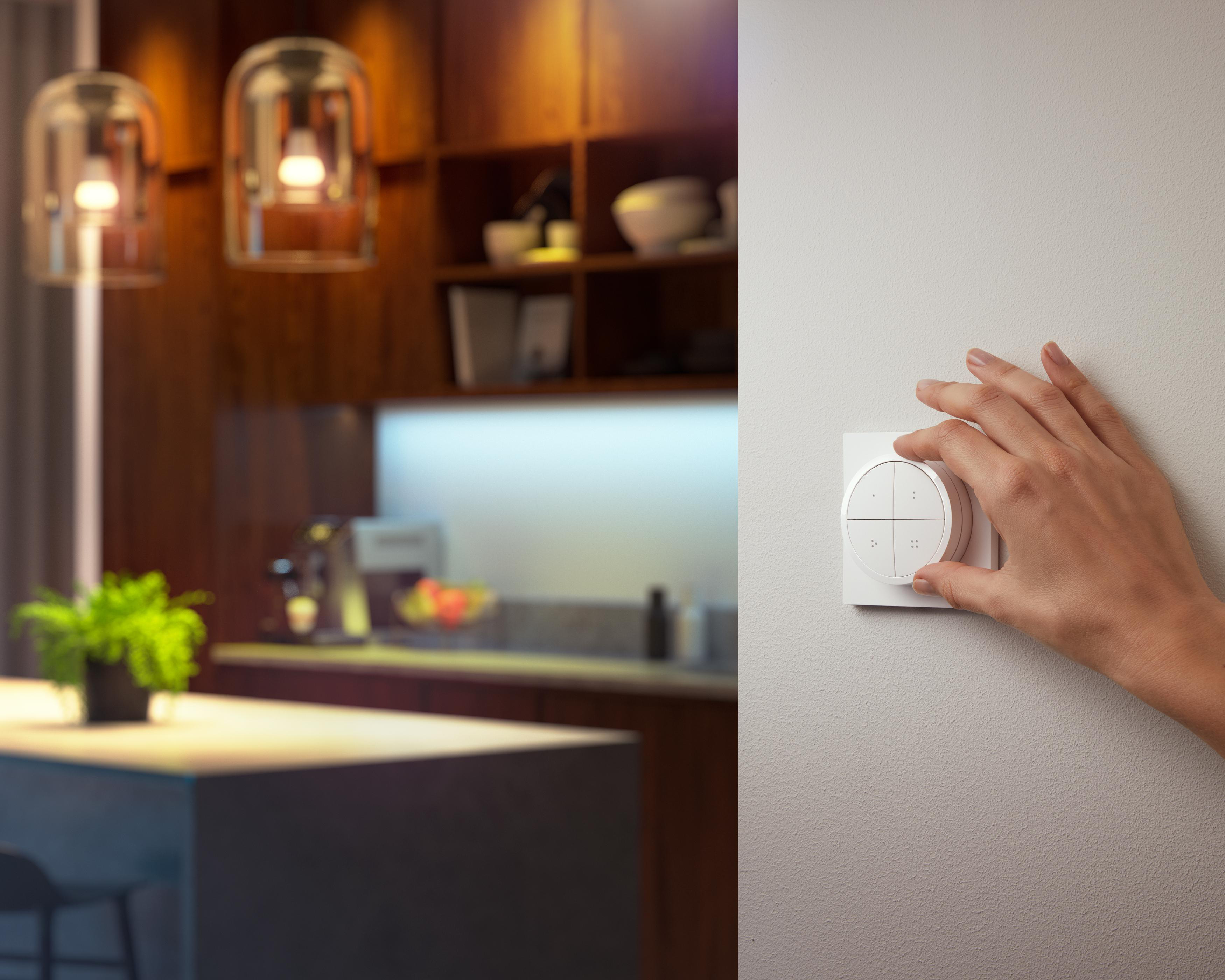 Eine Hand, die einen weißen Lichtschalter an der Wand einstellt. Hintergrund ist eine Küche.