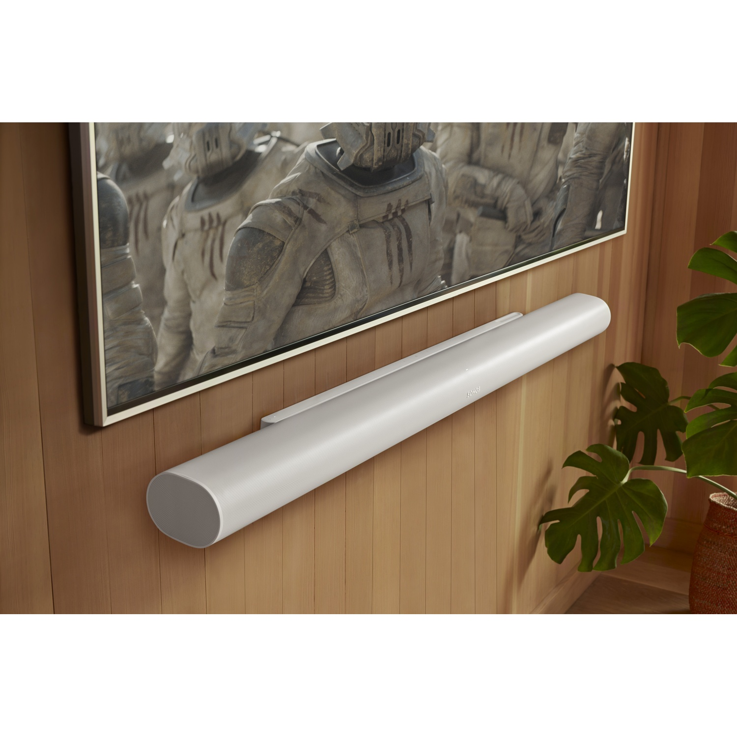 Una soundbar bianca montata a parete, sotto un'immagine incorniciata. Sfondo parete in legno.