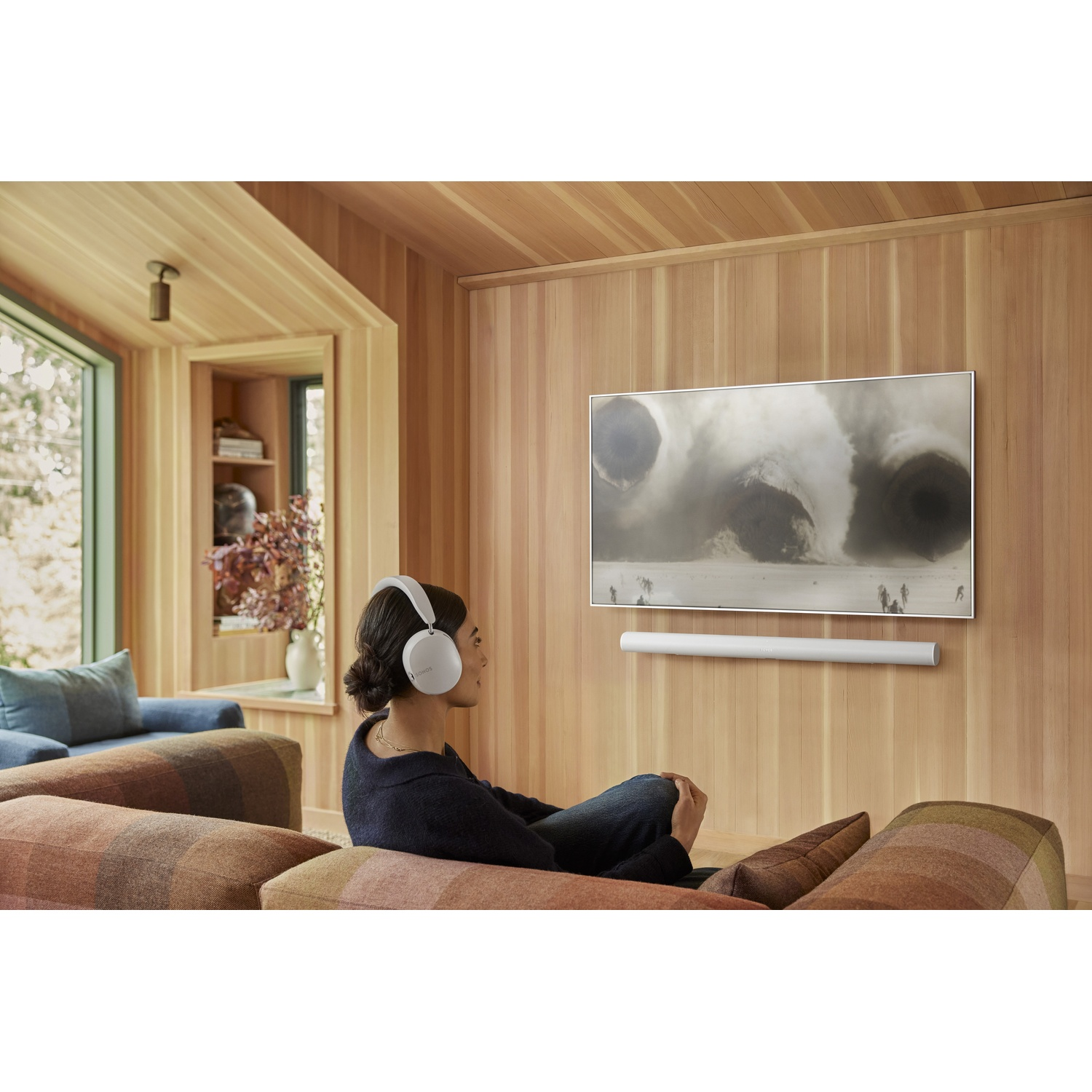 Donna con cuffie guarda la TV. Pannelli in legno chiaro decorano la stanza. Una soundbar bianca è sotto la TV.