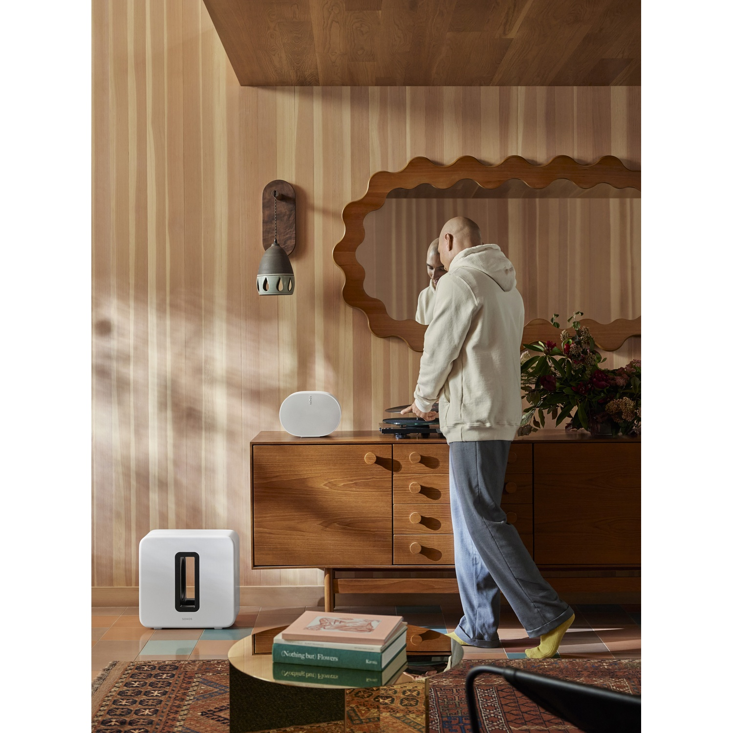 Un uomo è in piedi vicino a una console di legno. Un altoparlante bianco e un subwoofer sono nella stanza.