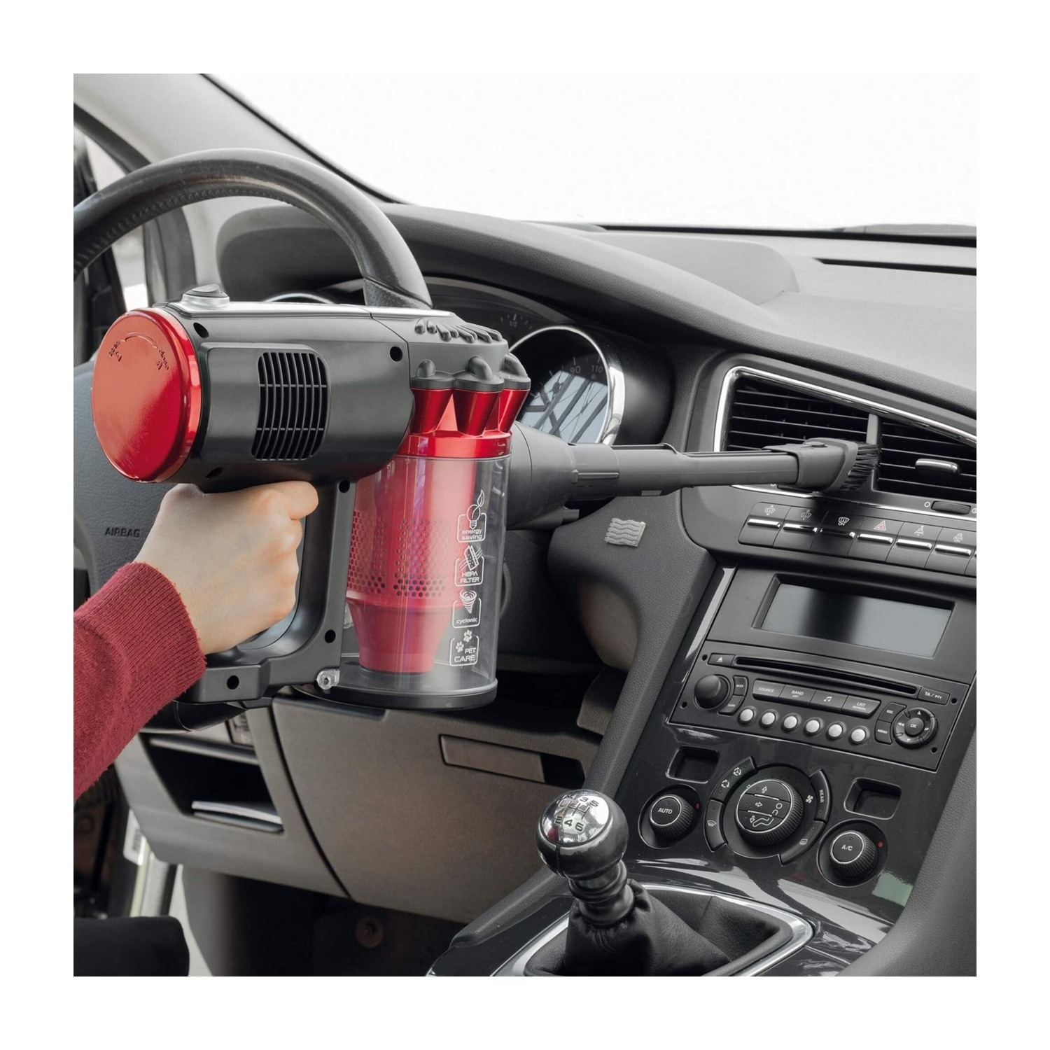 Una mano che tiene un aspirapolvere rosso e nero all'interno di un'auto.