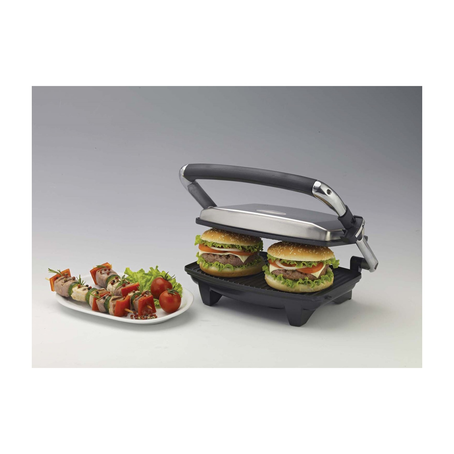Una piastra per panini con due hamburger e un piatto di cibo. Gli hamburger sono sulla piastra.