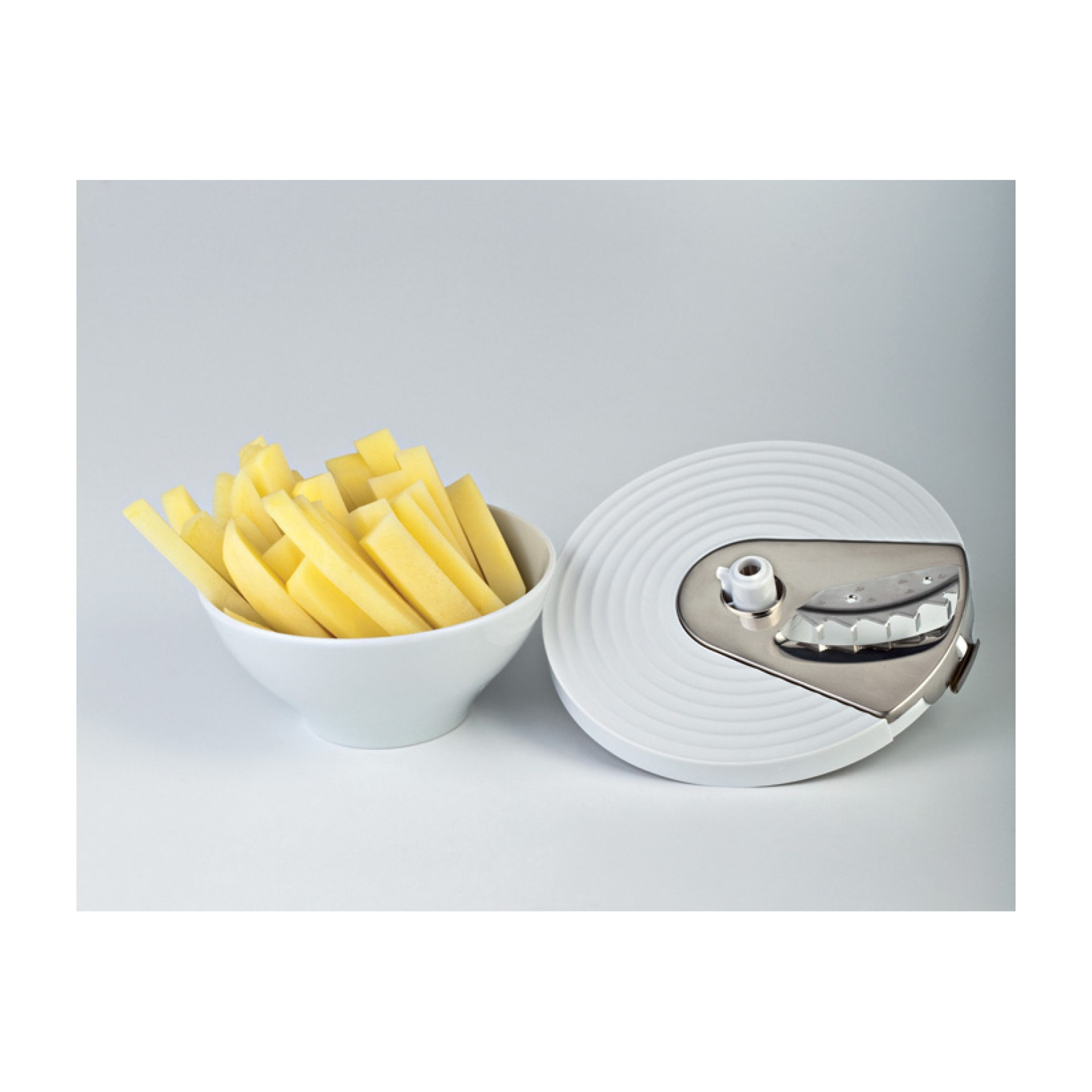 Ciotola di patatine fritte accanto a un accessorio per robot da cucina bianco su superficie bianca.