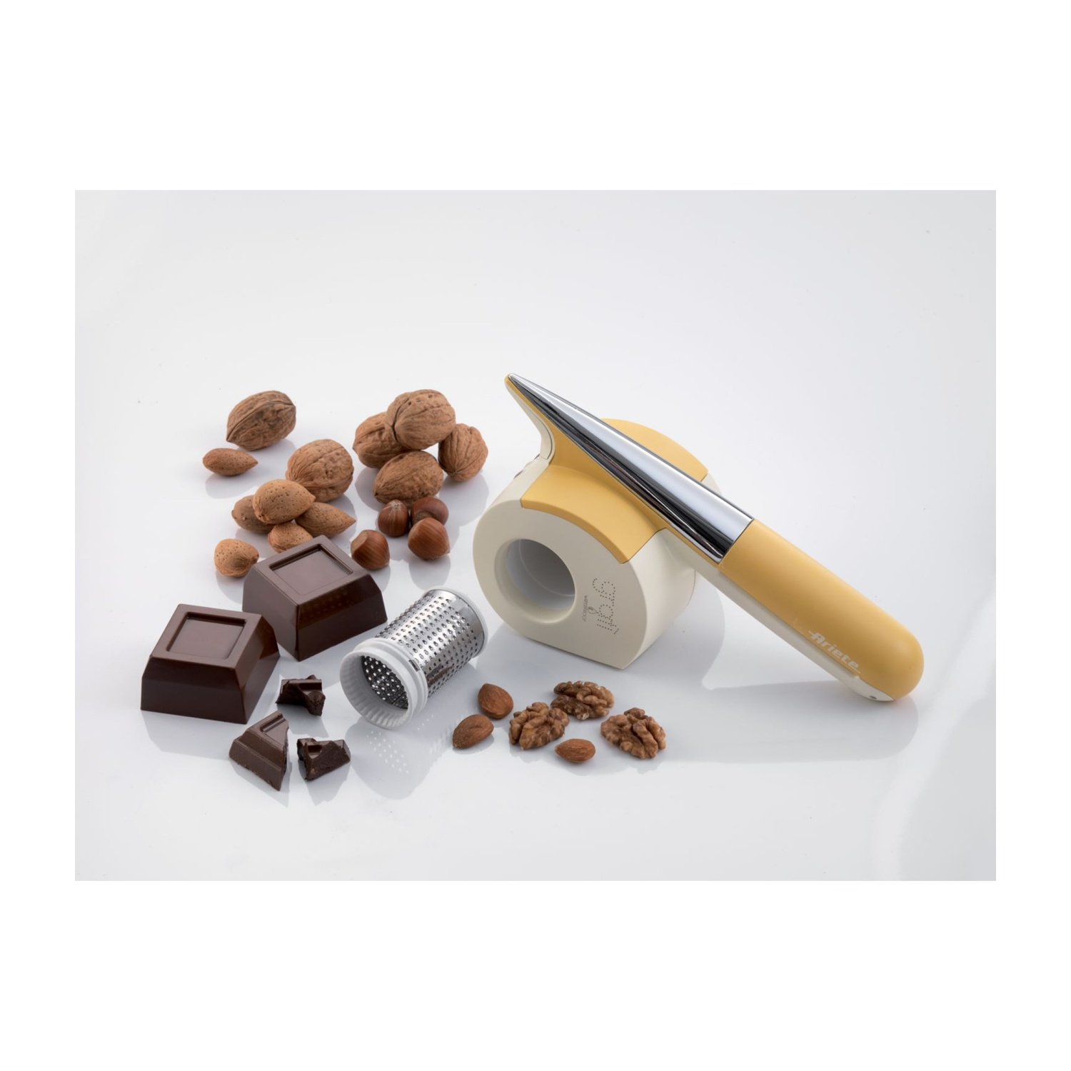 Una grattugia, pezzi di cioccolato, noci, mandorle e nocciole su superficie bianca.