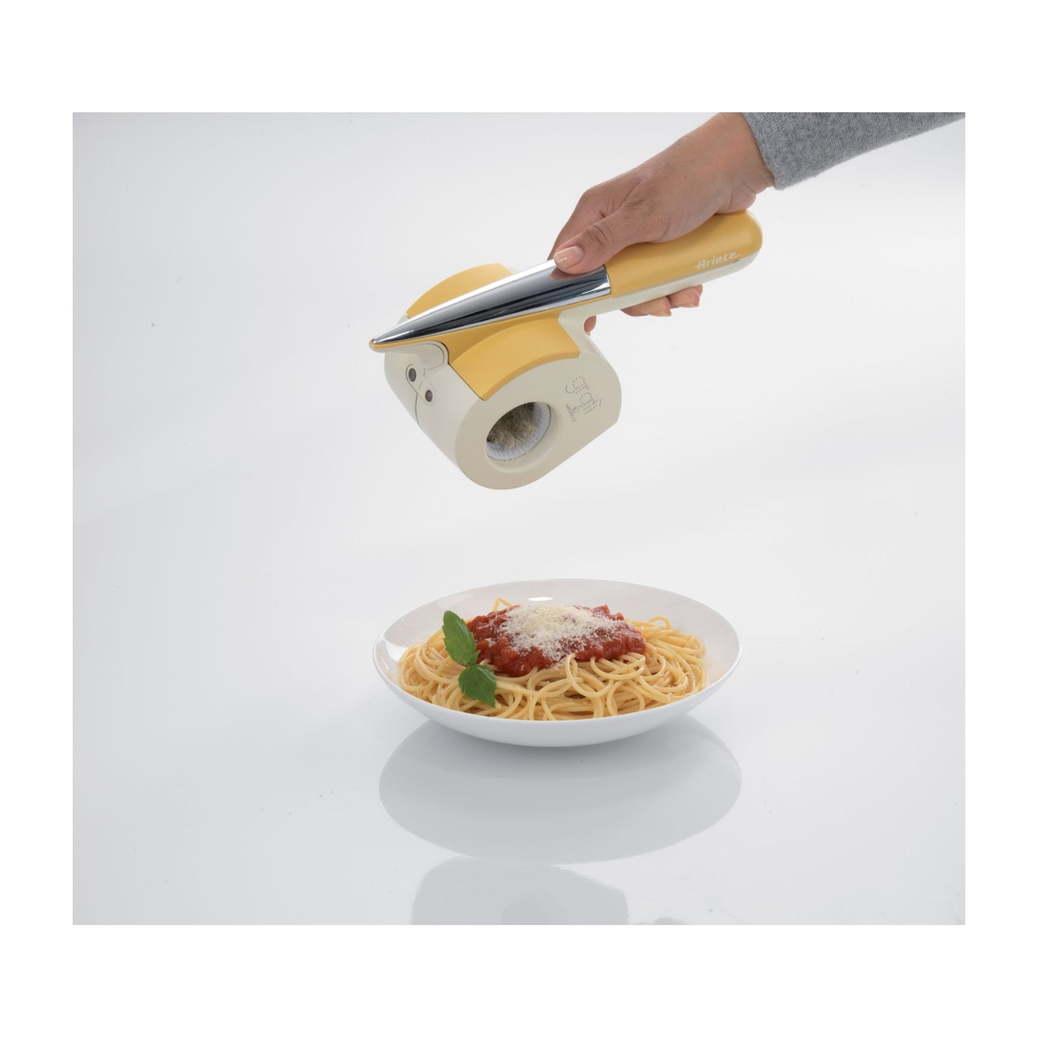 Mano che grattugia formaggio su un piatto di spaghetti. Si usa una grattugia gialla.