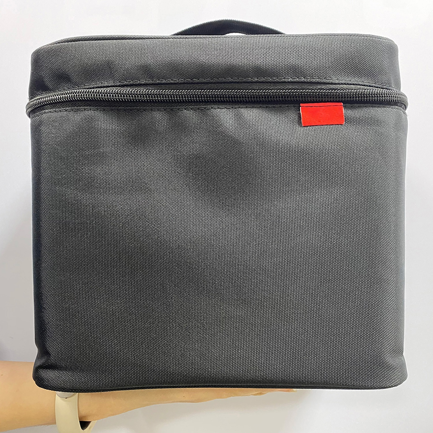 Una borsa nera con un'etichetta rossa. La borsa è di forma quadrata e ha una cerniera nella parte superiore.