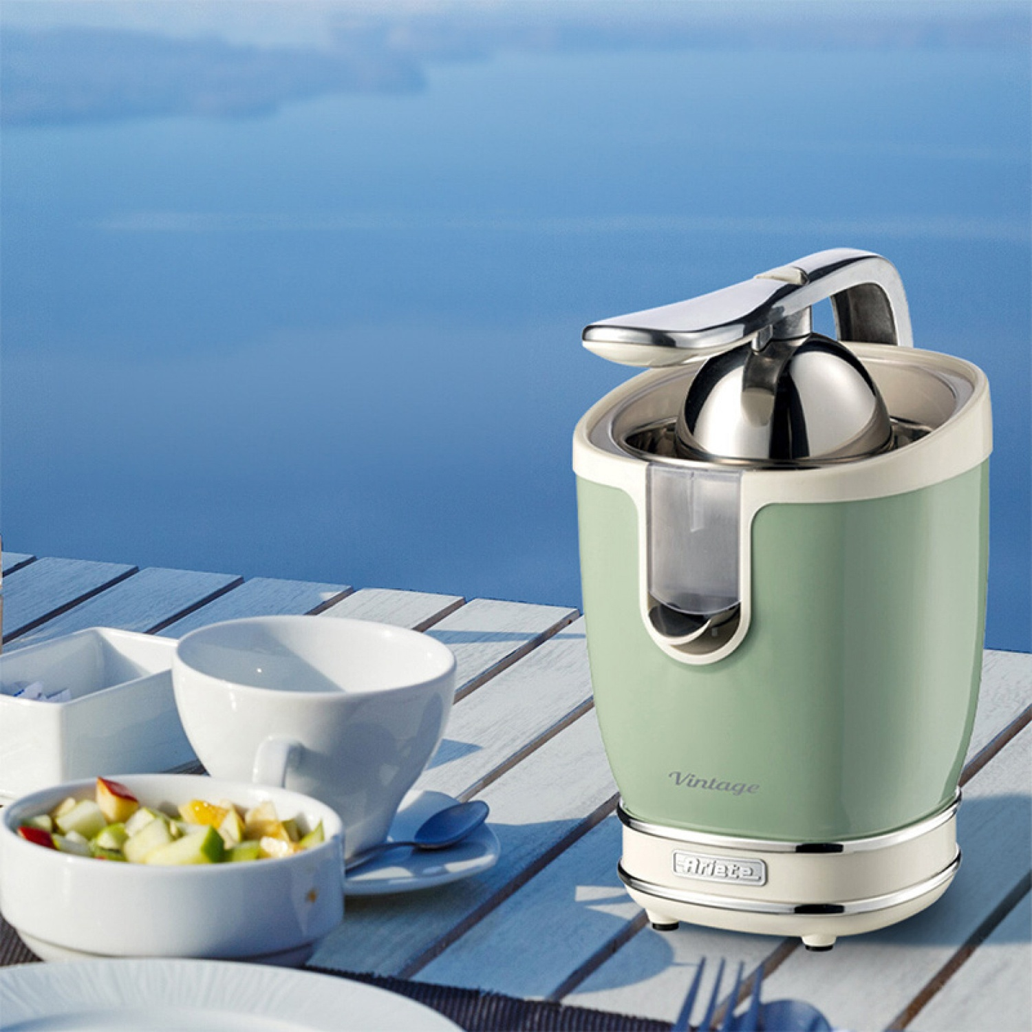 Spremiagrumi verde e bianco, ciotola di frutta, tazza e sfondo oceanico.