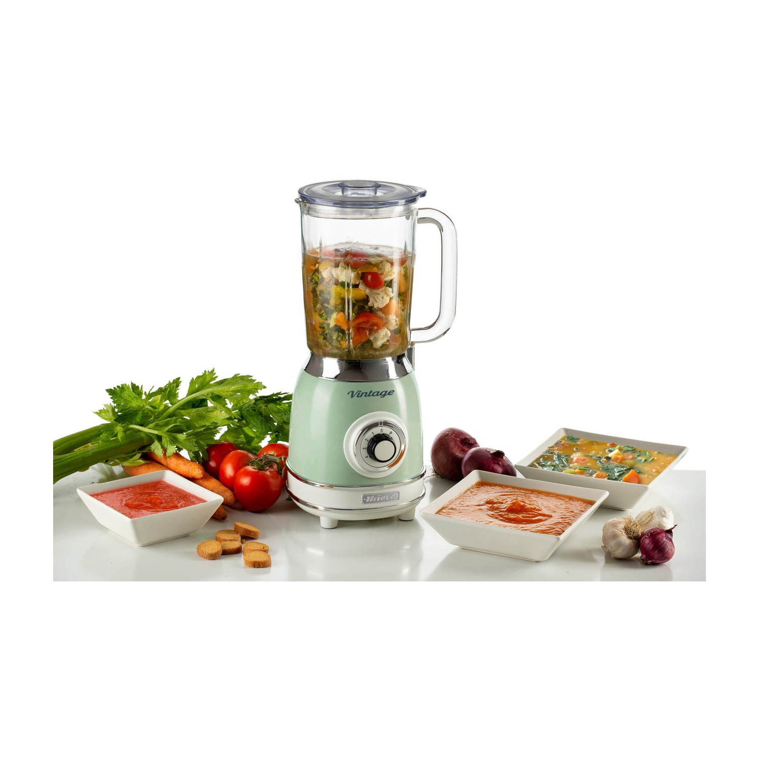 Un frullatore in stile vintage con verdure all'interno, accanto a ciotole di salsa e prodotti freschi.