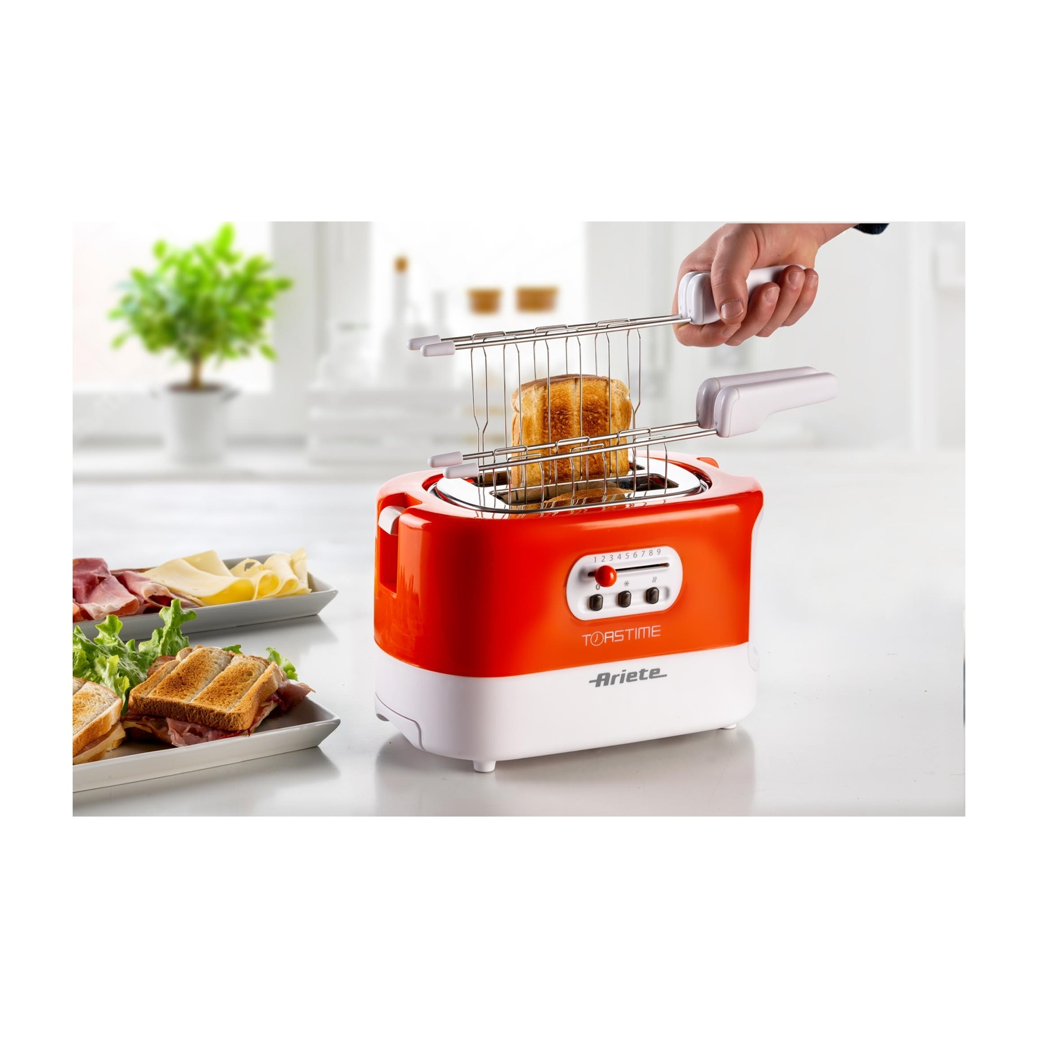 Tostapane rosso e bianco con toast all'interno. Mano che solleva il toast. Superficie bianca.