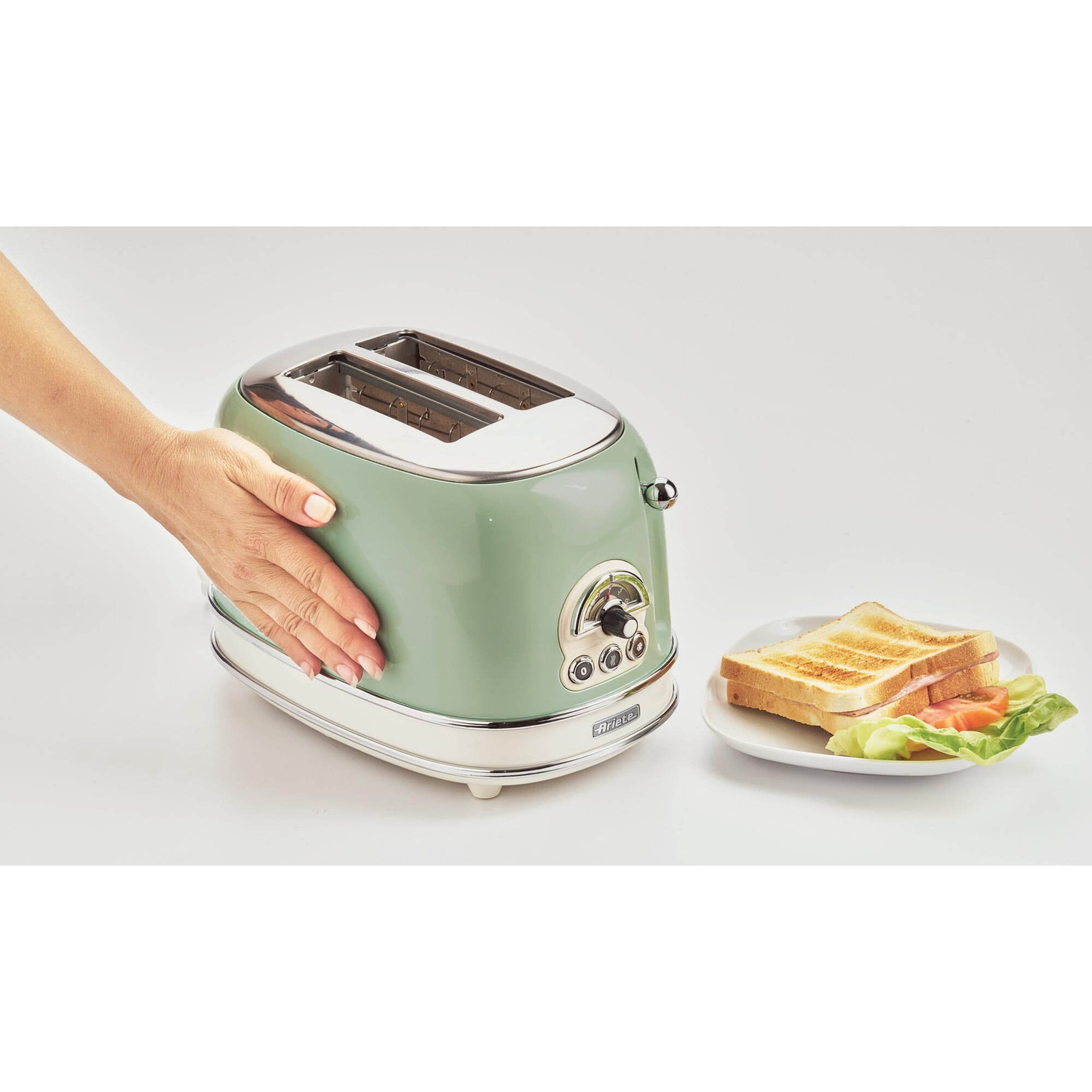 Un tostapane verde e bianco con una mano che lo tocca e toast su un piatto.