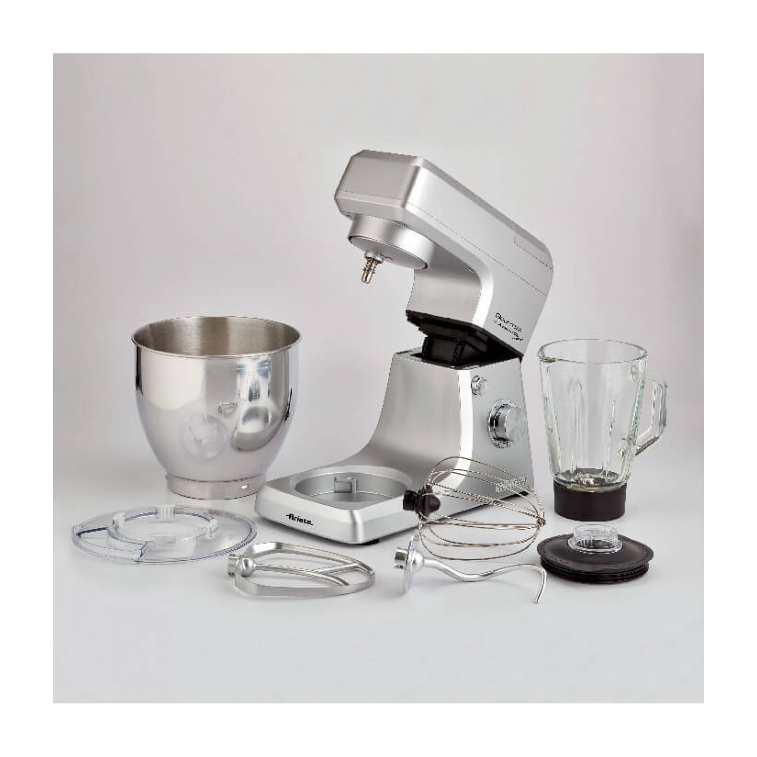 Robot da cucina argentato con accessori, un barattolo di vetro e una ciotola in acciaio inox su sfondo bianco.