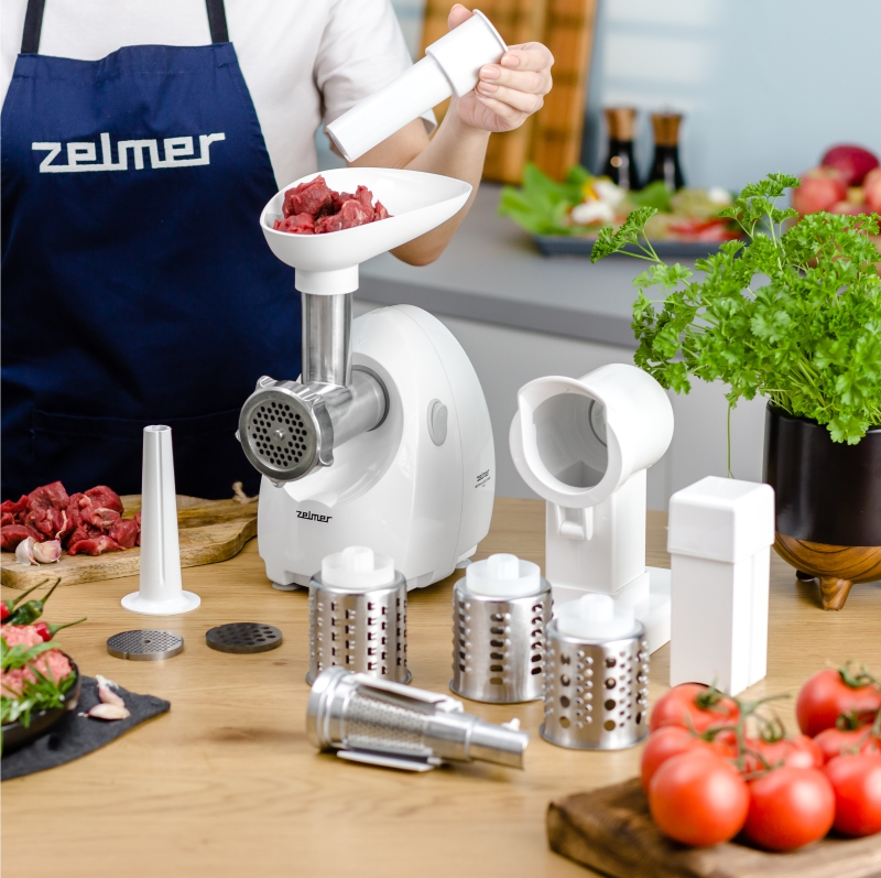 Biały robot kuchenny z różnymi przystawkami i składnikami na drewnianym stole.