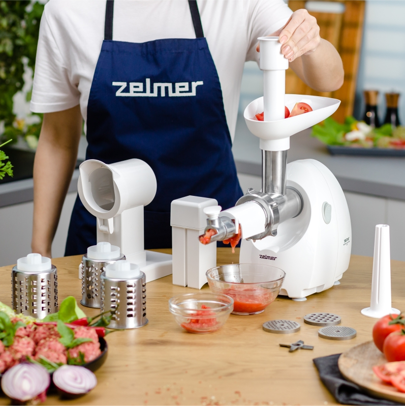 Biały robot kuchenny z różnymi przystawkami i osobą trzymającą pomidora.