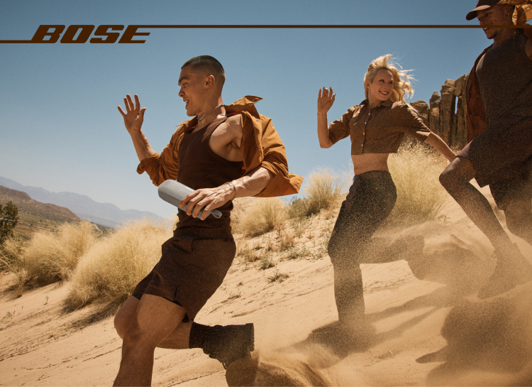 Drei Personen rennen in der Wüste mit einem Bose-Lautsprecher, Staub in der Luft und dem Bose-Logo.