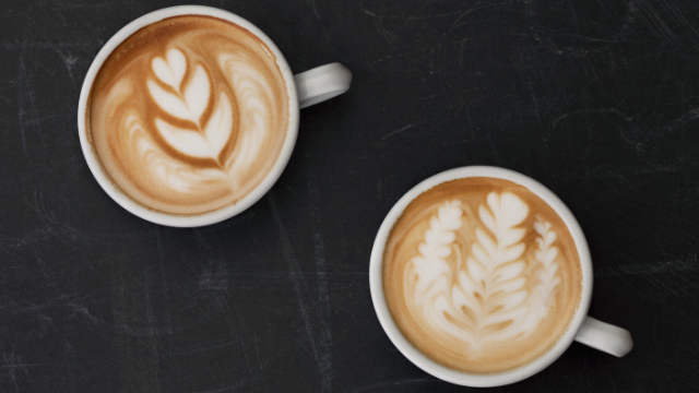 Két latte art kávé fekete felületen, levélmintákkal.