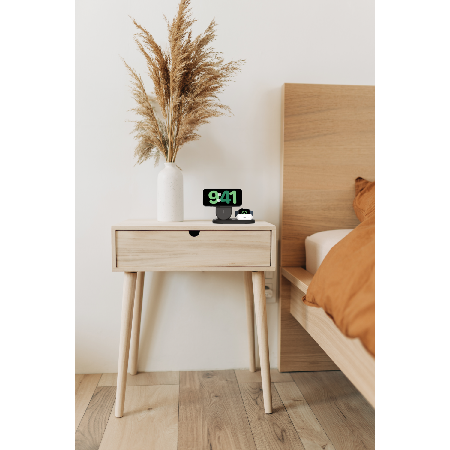 Table de chevet avec vase, station de recharge et lit avec couverture orange.