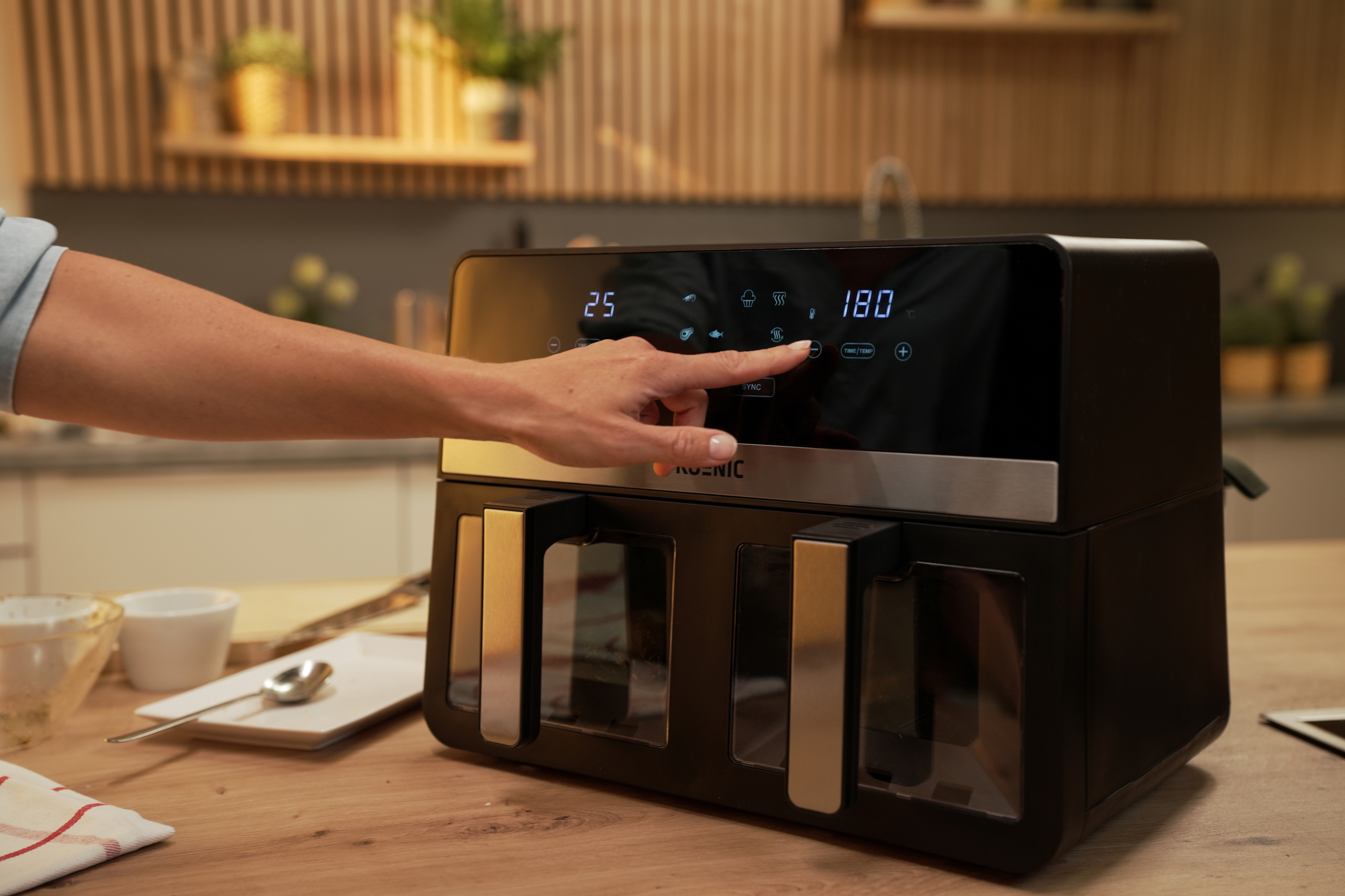 Dłoń naciskająca przycisk na czarnej frytkownicy powietrznej z cyfrowym wyświetlaczem.