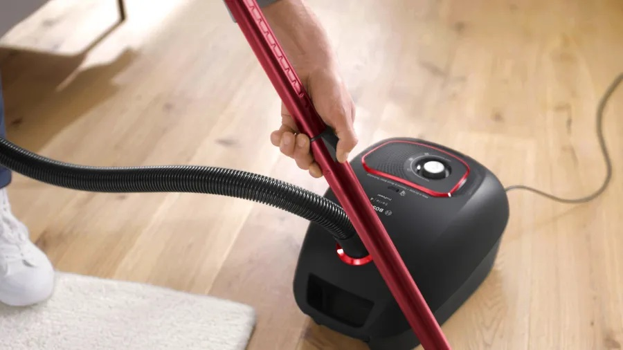 Osoba używająca odkurzacza na drewnianej podłodze z dywanem.