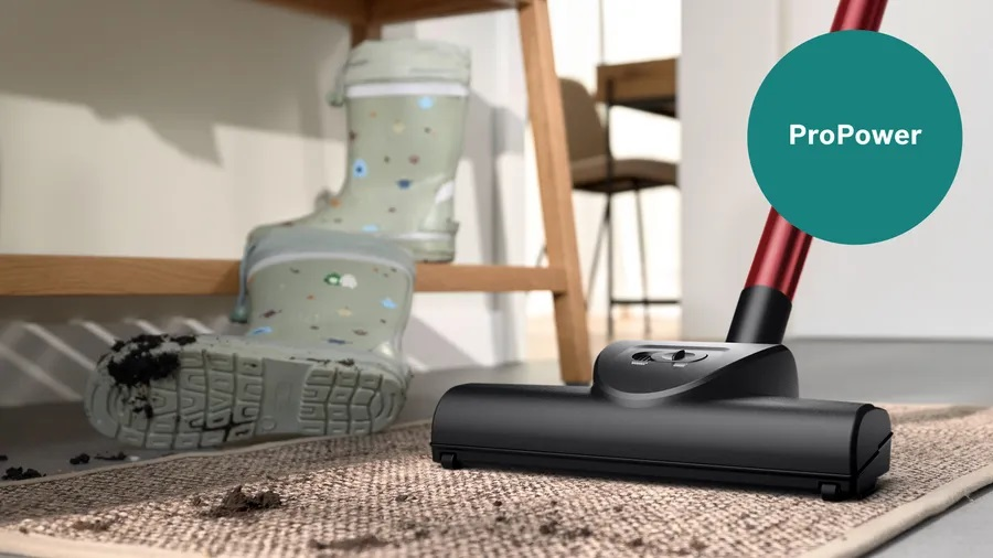Głowica odkurzacza na dywanie, z błotem i butami. Tekst mówi 'ProPower' w zielonym kole.