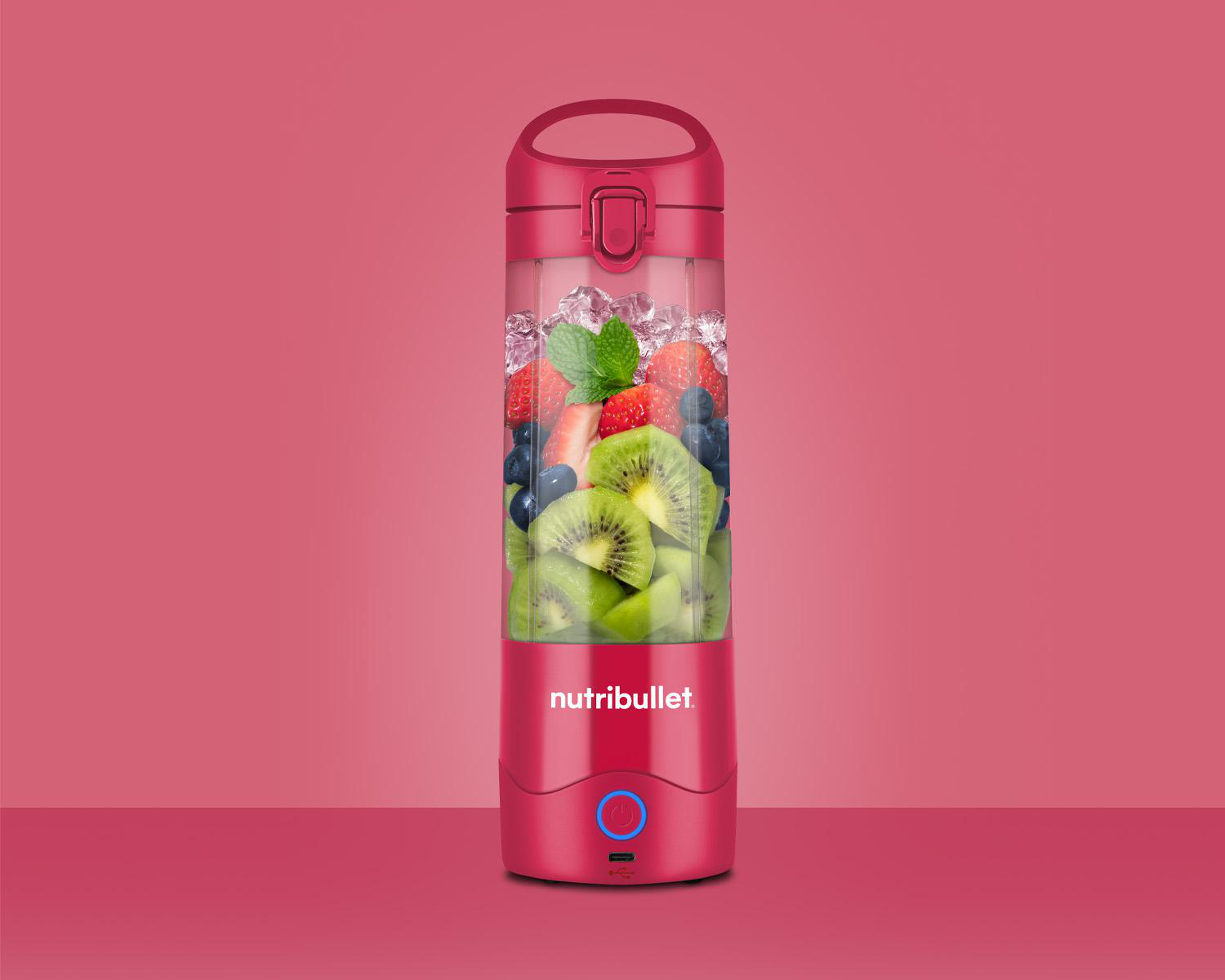 Eine rote Nutribullet-Mixerflasche gefüllt mit Eis, Erdbeeren, Blaubeeren und Kiwischeiben.
