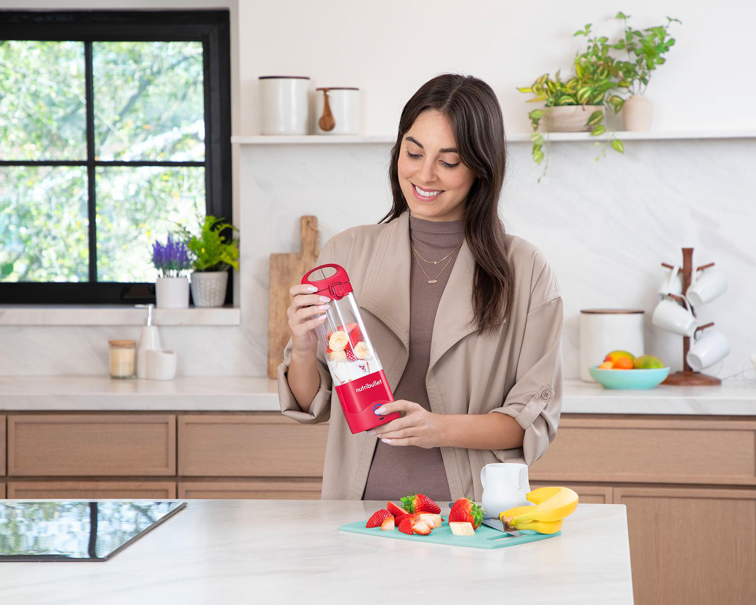 Frau macht Smoothie mit rotem und transparentem Mixer in weißer Küche.