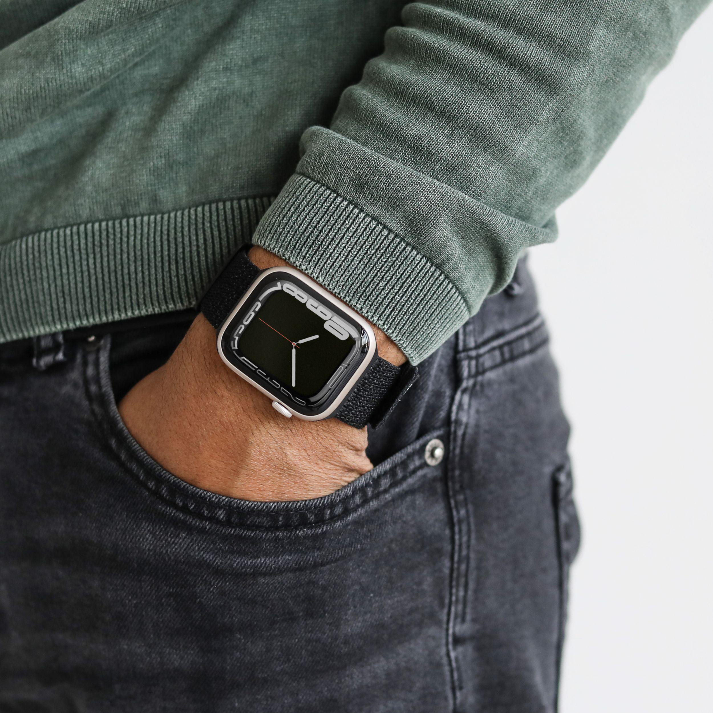 Das Handgelenk einer Person mit einer schwarzen Uhr und einem schwarzen Armband in einer Tasche.