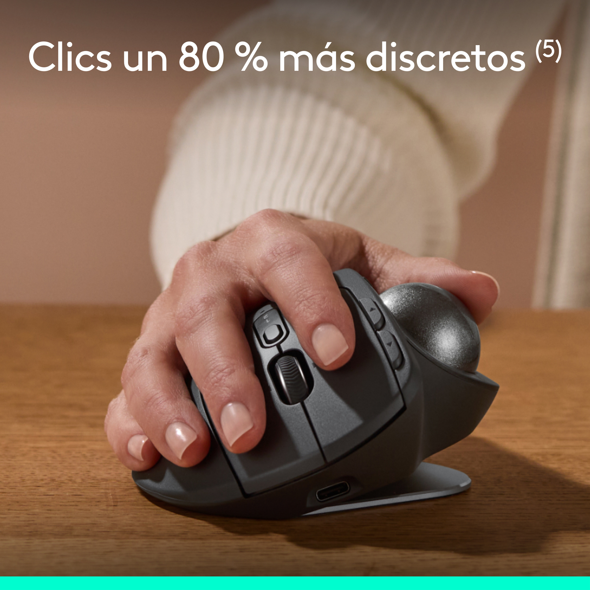 Mano usando un ratón trackball gris en un escritorio de madera. Texto arriba.