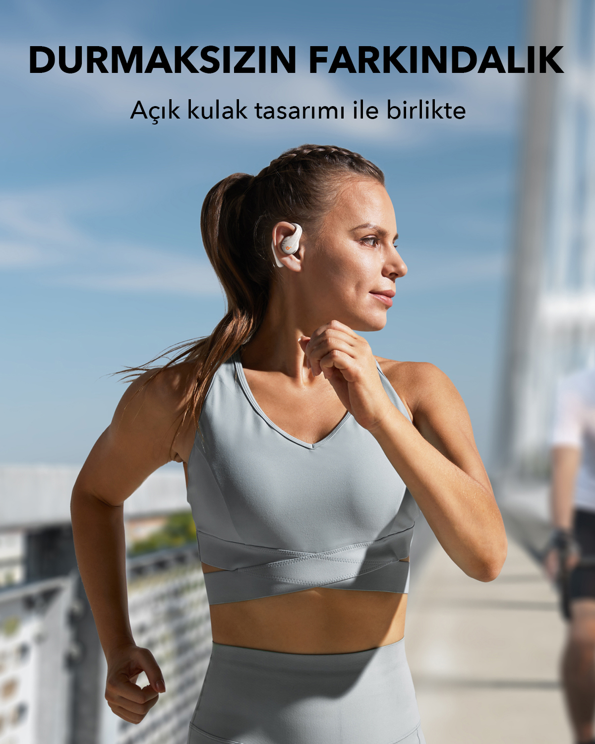 Beyaz kulaklık takan koşan kadın. Gri bir spor sütyeni giyiyor ve güneşli bir ortamda.