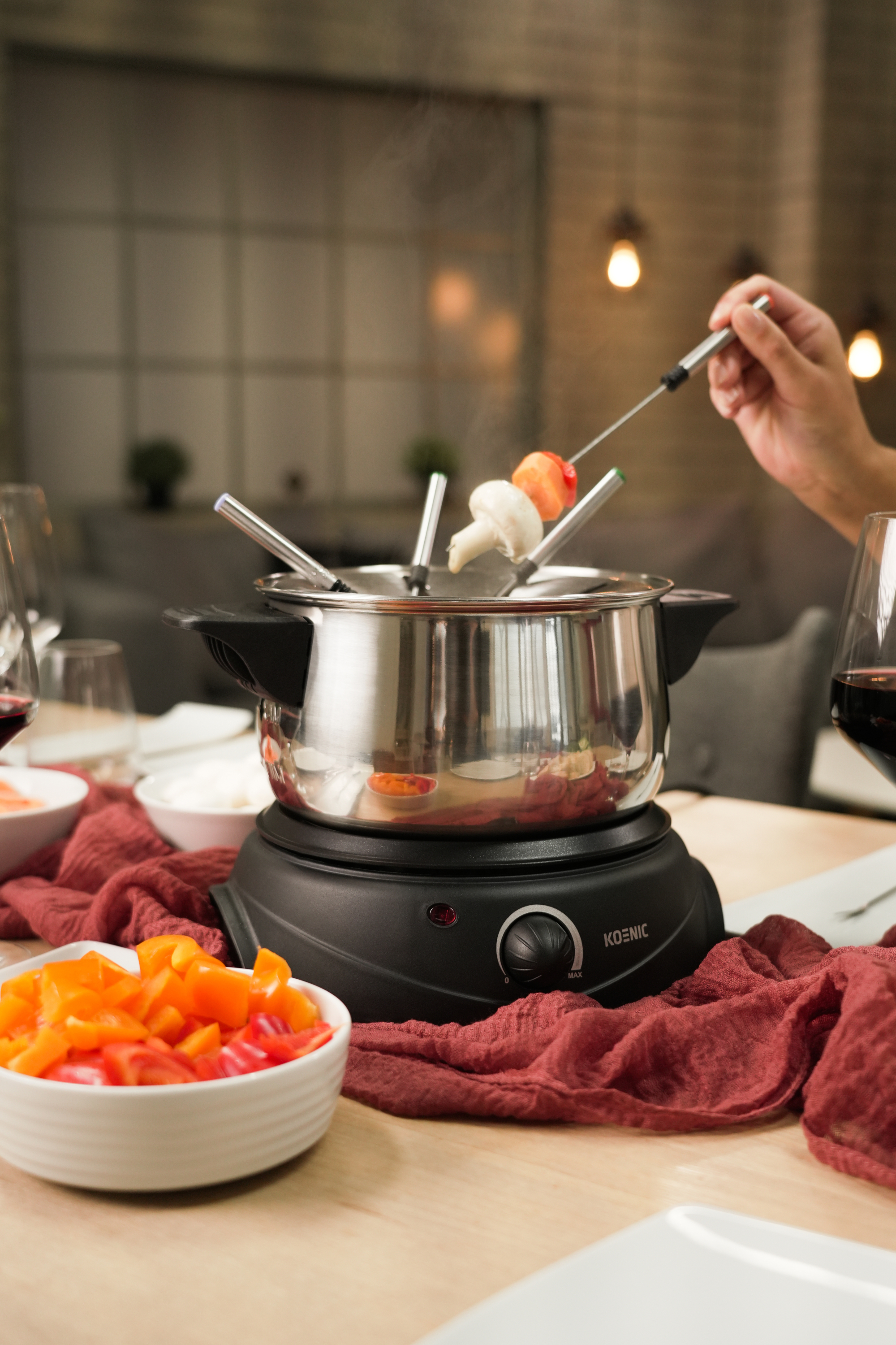 Garnek do fondue na stole z szaszłykami, warzywami i ręką z szaszłykiem.