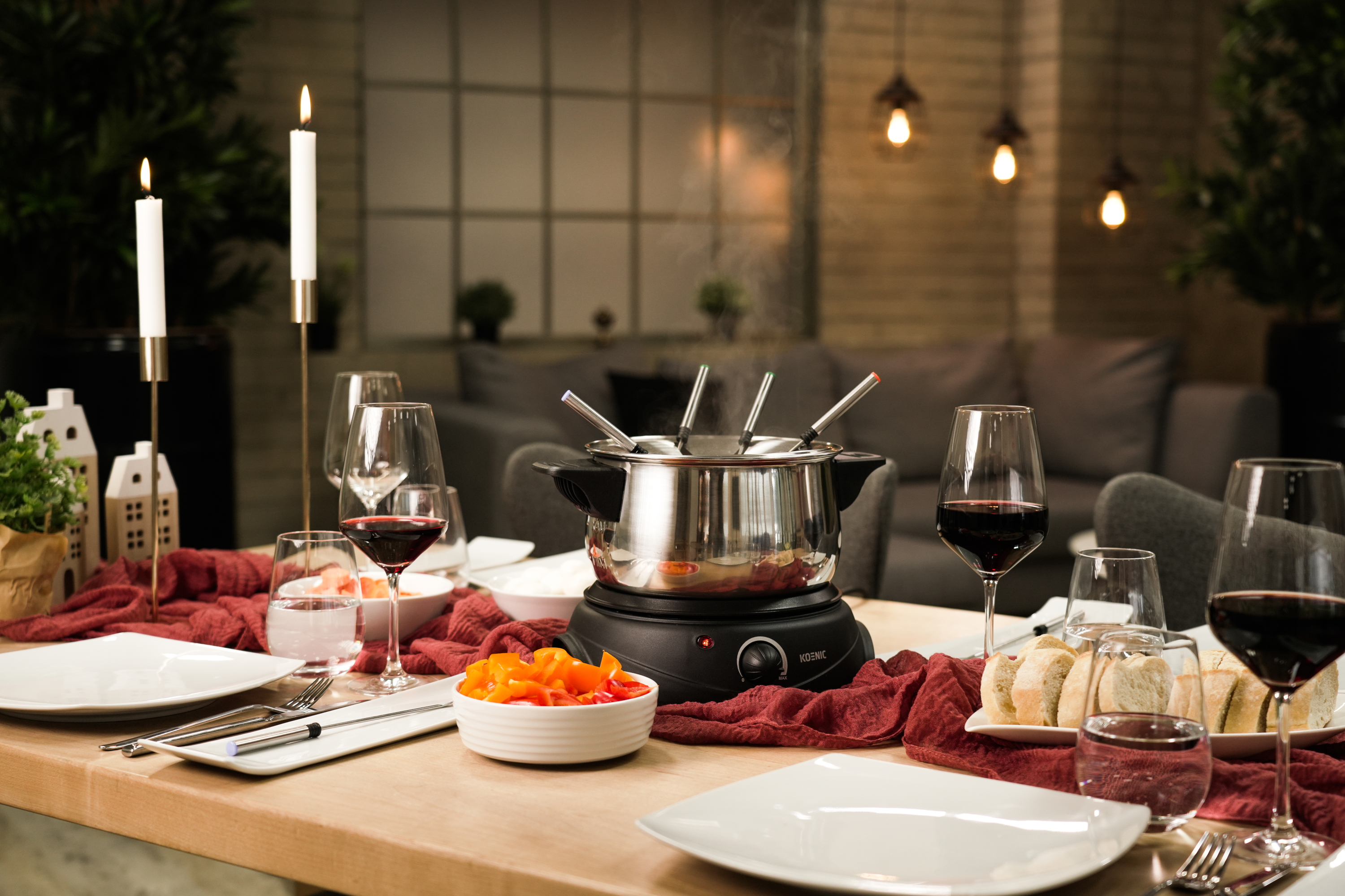 Stół jadalny nakryty do fondue z świecami, winem i jedzeniem.