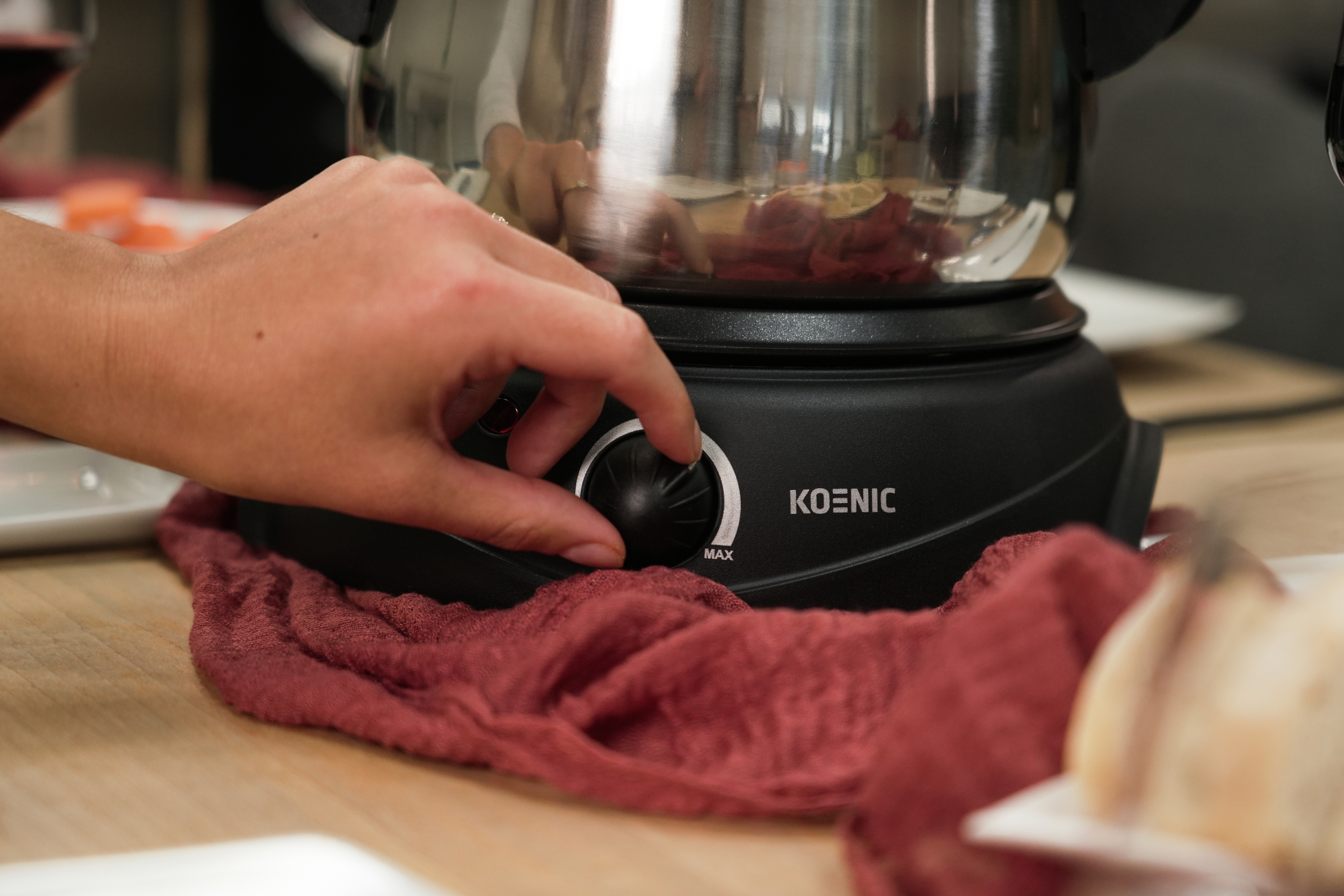 Ręka kręci pokrętłem na czarnym garnku do fondue Koenic na czerwonej szmatce.