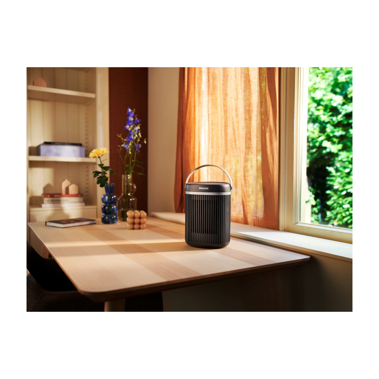 Altoparlante Philips nero su un tavolo di legno. Finestra e scaffalatura sullo sfondo. Scena soleggiata.