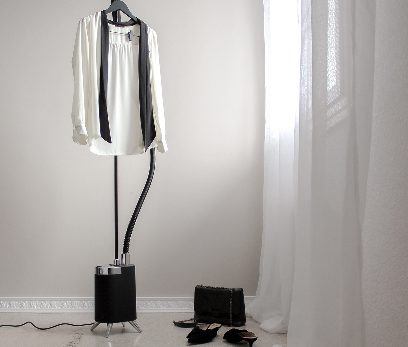 Chemise blanche, cravate noire. Sac noir, chaussures au sol. Défroisseur au sol.