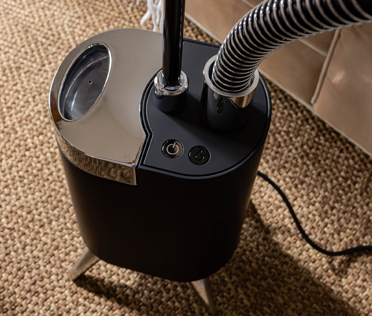 Vapeur de vêtements noir et argent avec tuyau flexible, sur surface marron texturée.