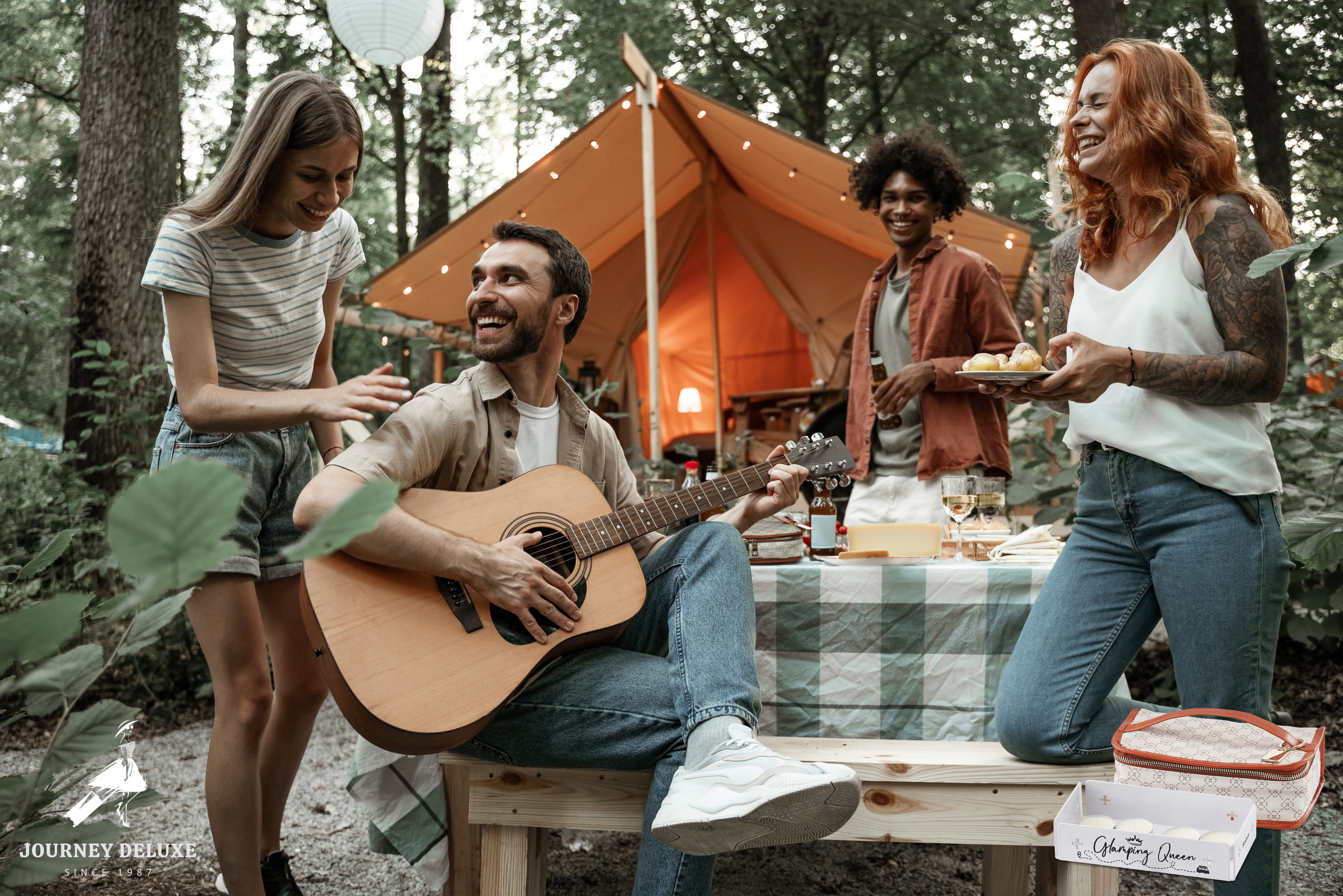 Un gruppo di amici in campeggio. Uno suona la chitarra, altri mangiano. Una tenda e alberi sullo sfondo.