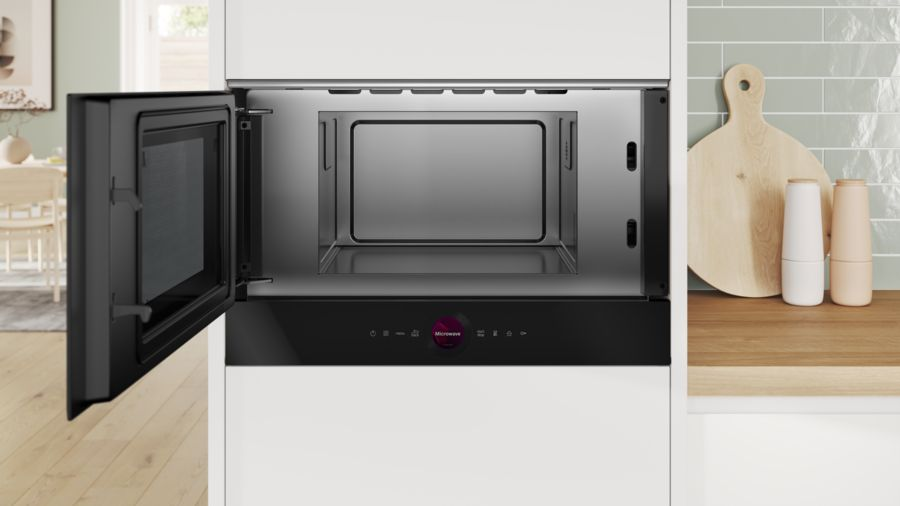 Horno microondas, abierto, en una cocina blanca. Interior negro. La puerta es negra.