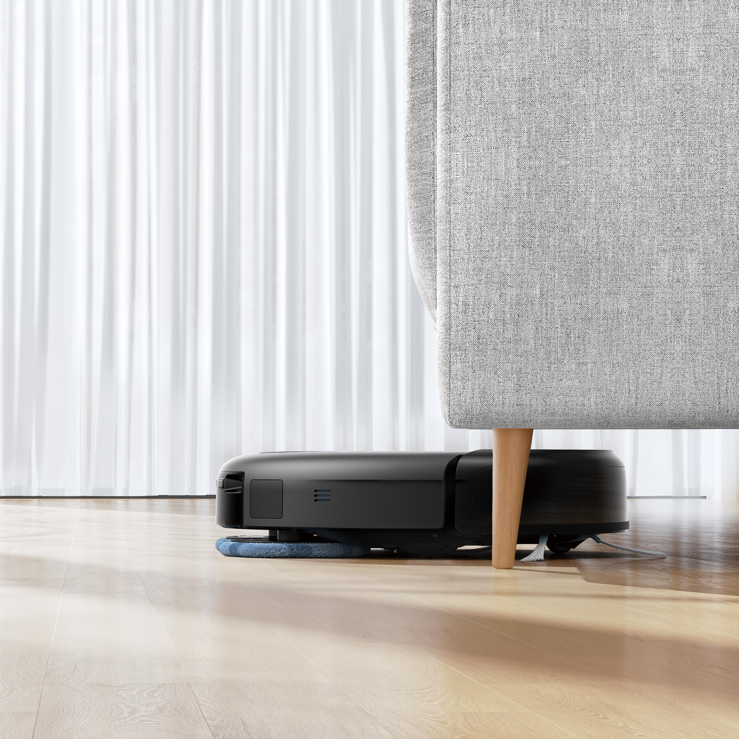 Roboter-Staubsauger unter einer Couch. Graue Couch, Holzboden und weiße Vorhänge.