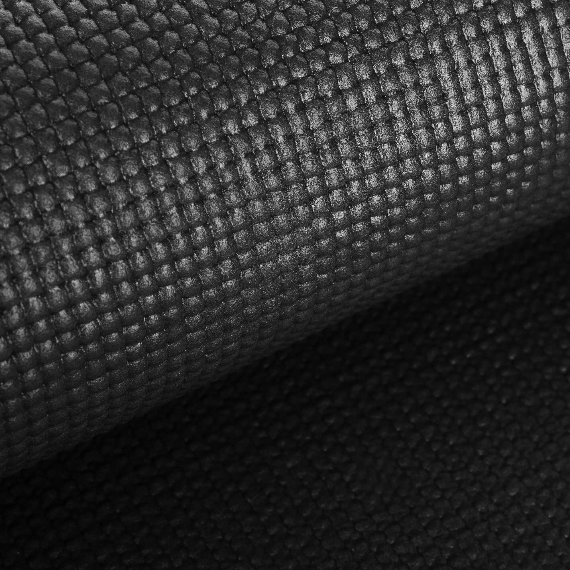 Czarna, teksturowana powierzchnia. Zwinięta, z wzorem kratki. Słabe oświetlenie.