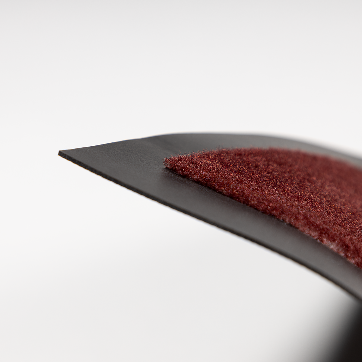 Nahaufnahme eines schwarzen, gebogenen Materials mit einer roten, strukturierten Oberfläche auf weißem Grund.