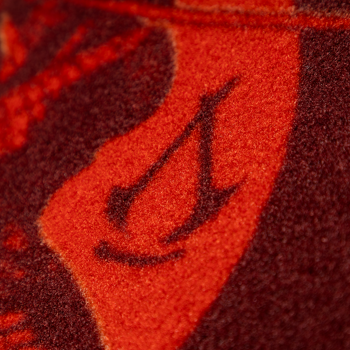 Nahaufnahme eines orangefarbenen und dunkelroten gemusterten Teppichs mit stilisiertem Design.