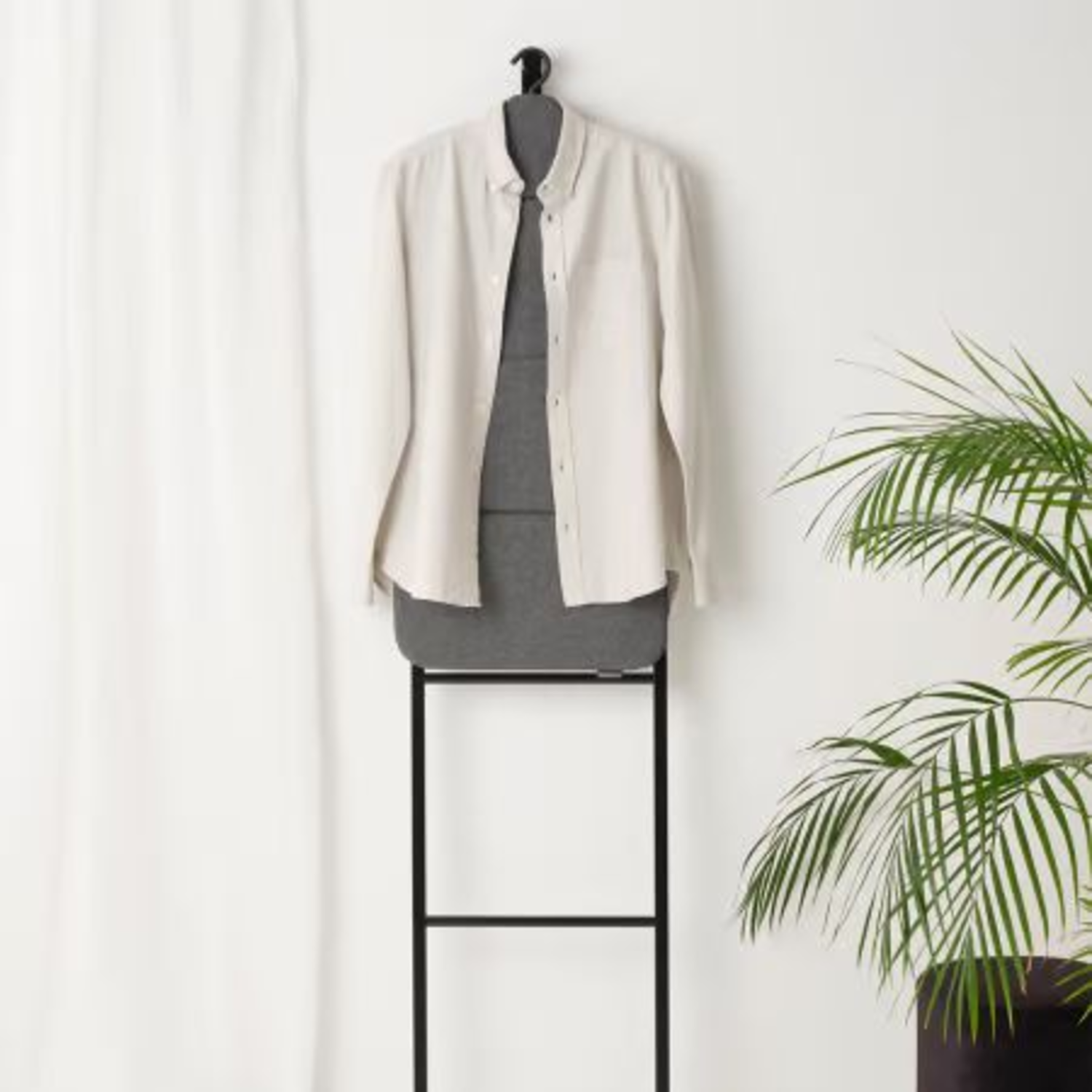 Wit overhemd en grijze top hangend aan een staand rek, met een plant.