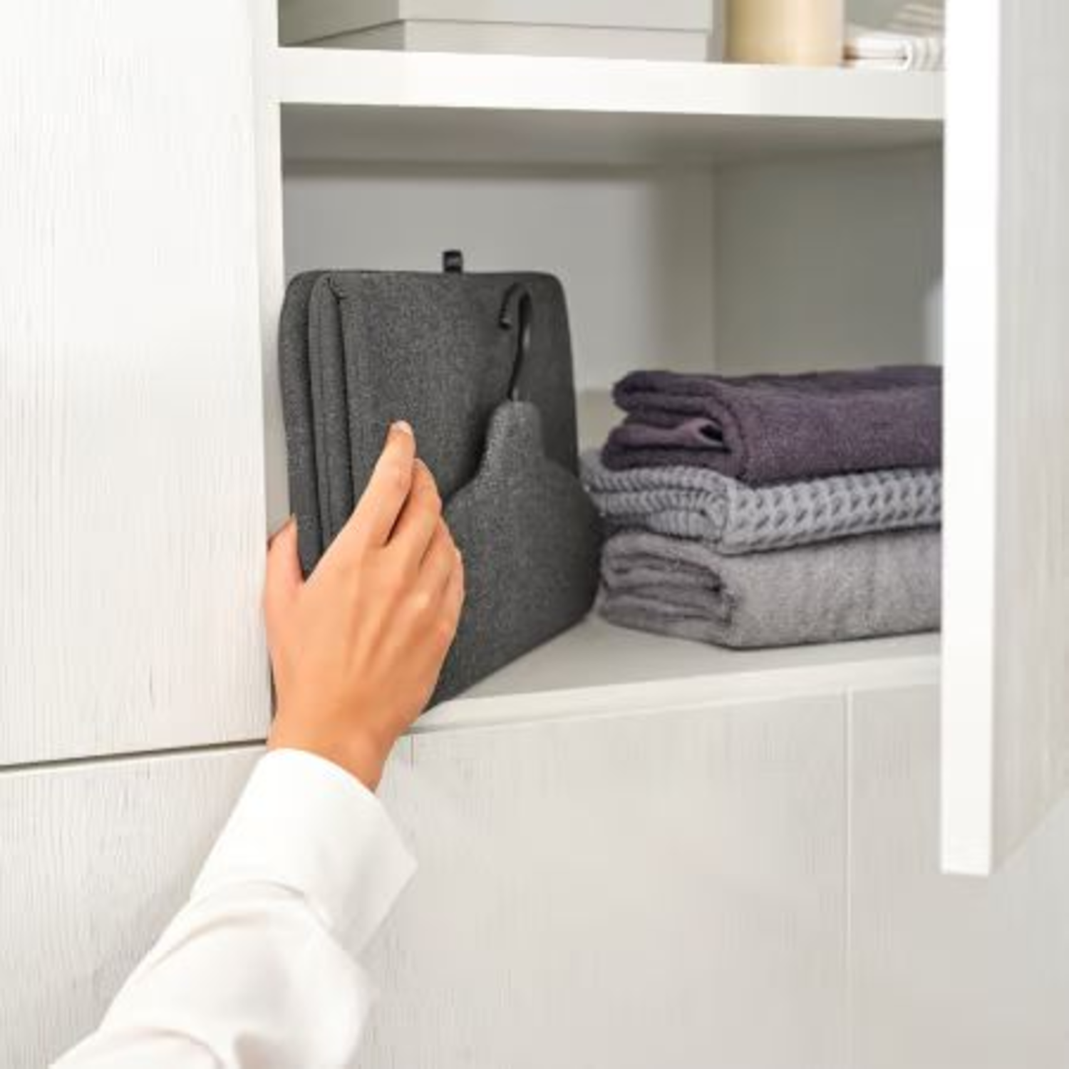 Een hand reikt in een kast om een ​​hanger te pakken, naast opgevouwen handdoeken.