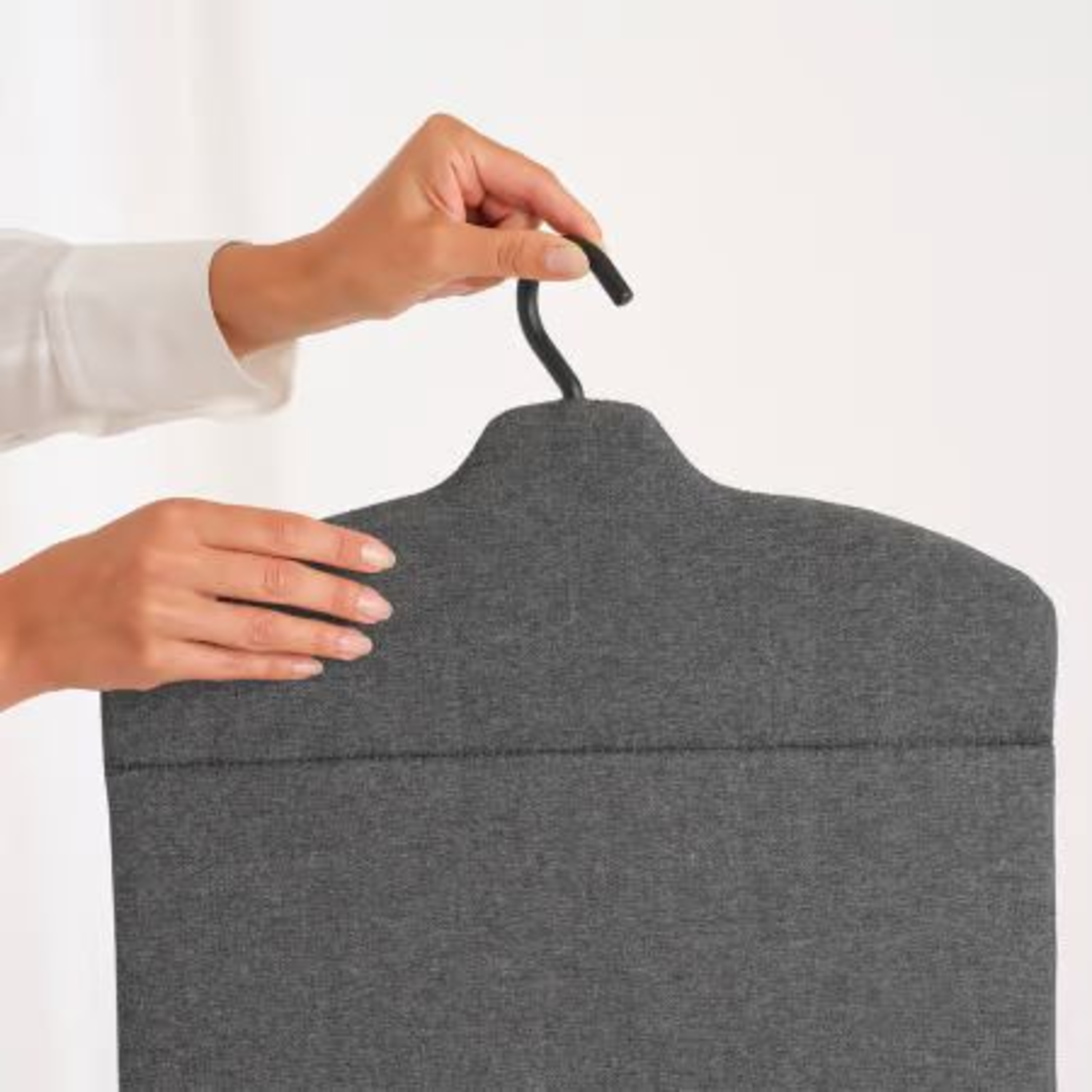Mains tenant un cintre en tissu gris sur fond blanc.